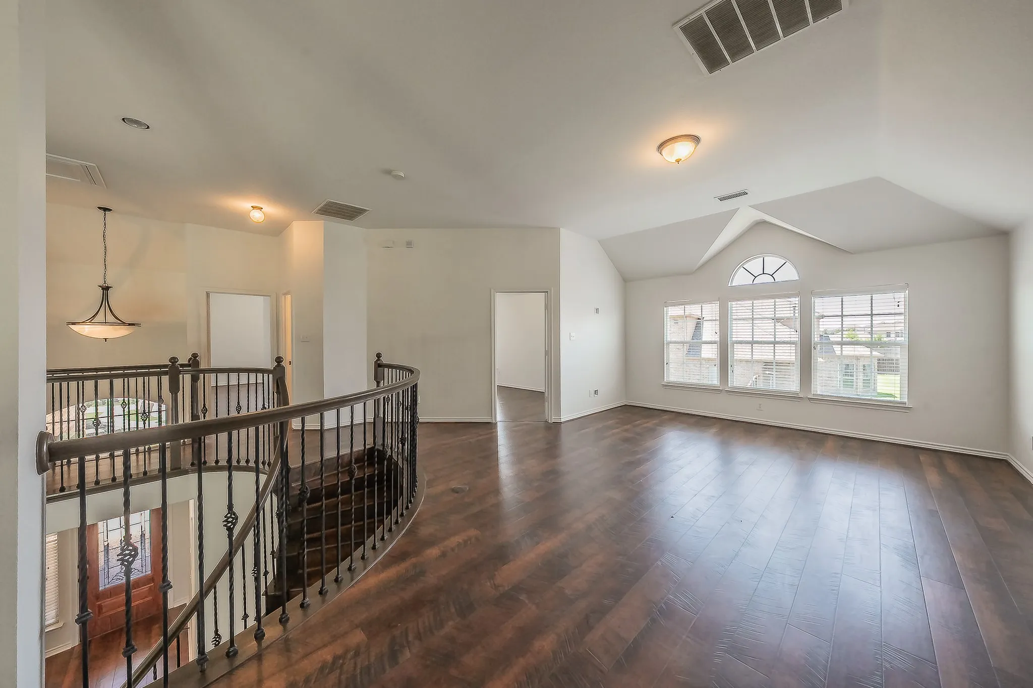 Spacious upper landing and loft area with hardwood floors, vaulted ceiling, arched windows, curved wrought iron railing overlooking the foyer below, and open views to multiple bedroom entries.