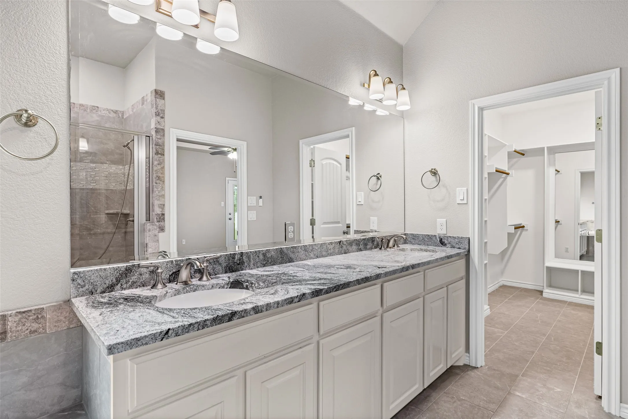 Dual vanity featuring undermount sinks, a patterned stone countertop, and brushed nickel fixtures