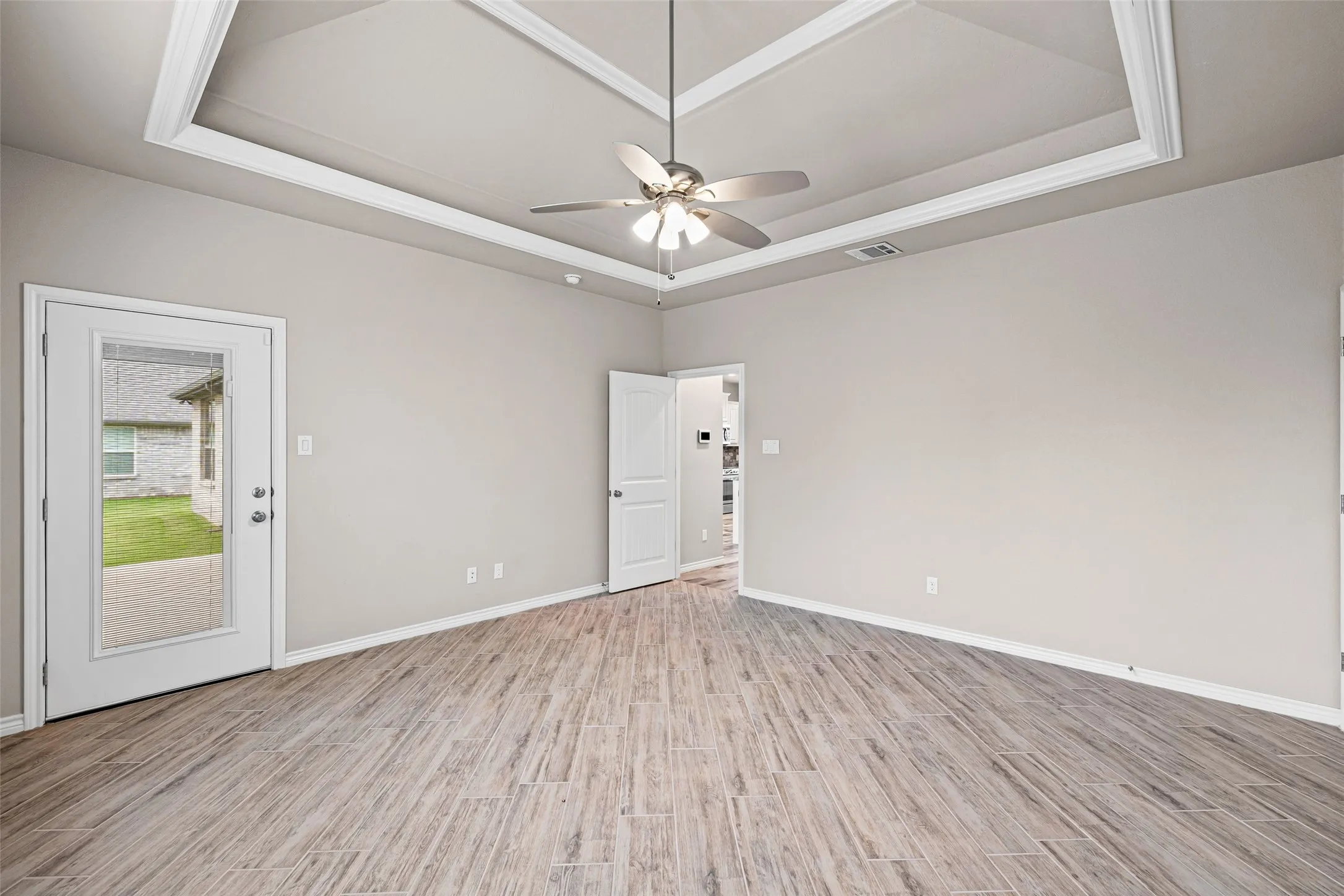 Spacious room featuring wood-finish flooring, a tray ceiling with a fan, and light neutral wall tones