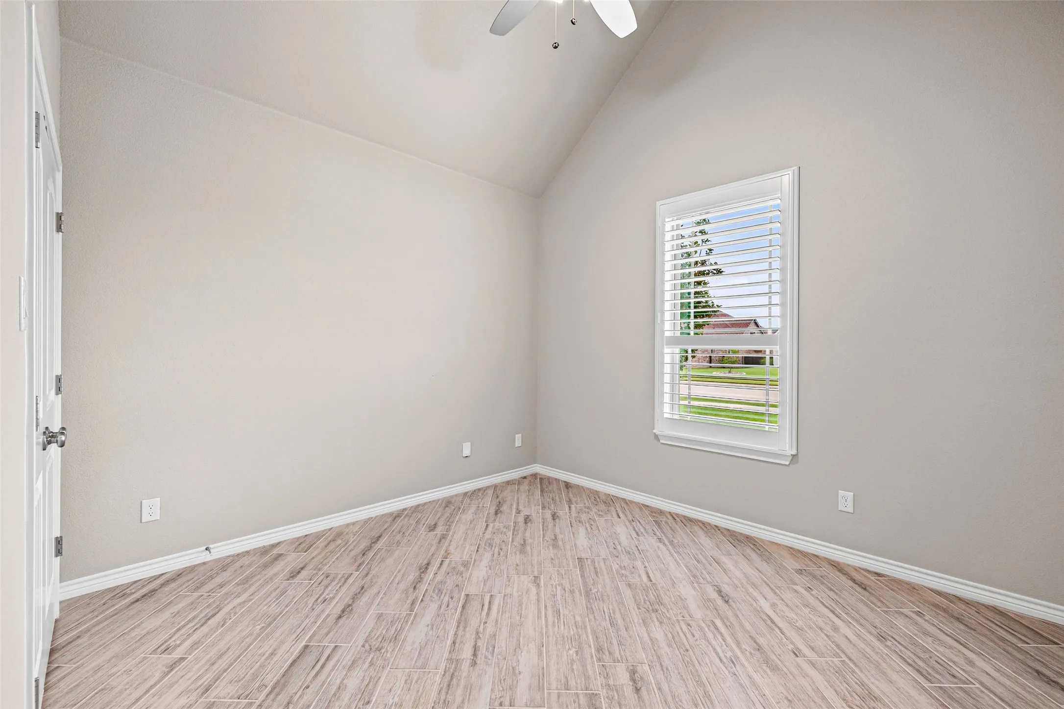 Interior room featuring vaulted ceilings, wood-finish flooring, and a window with white louvered blinds