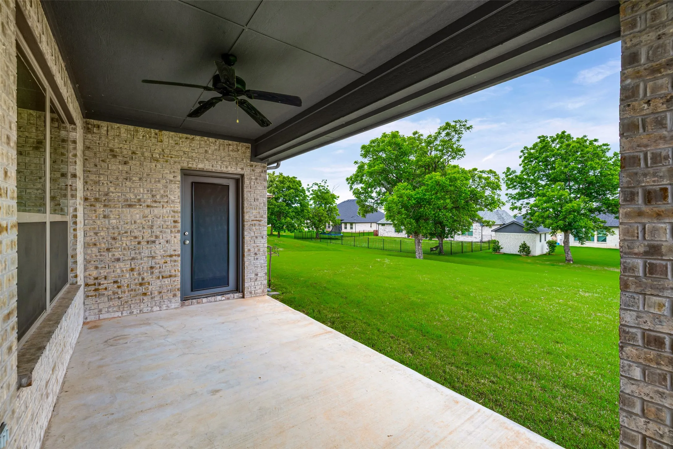 Covered patio with a concrete surface, brick exterior, and a ceiling fan