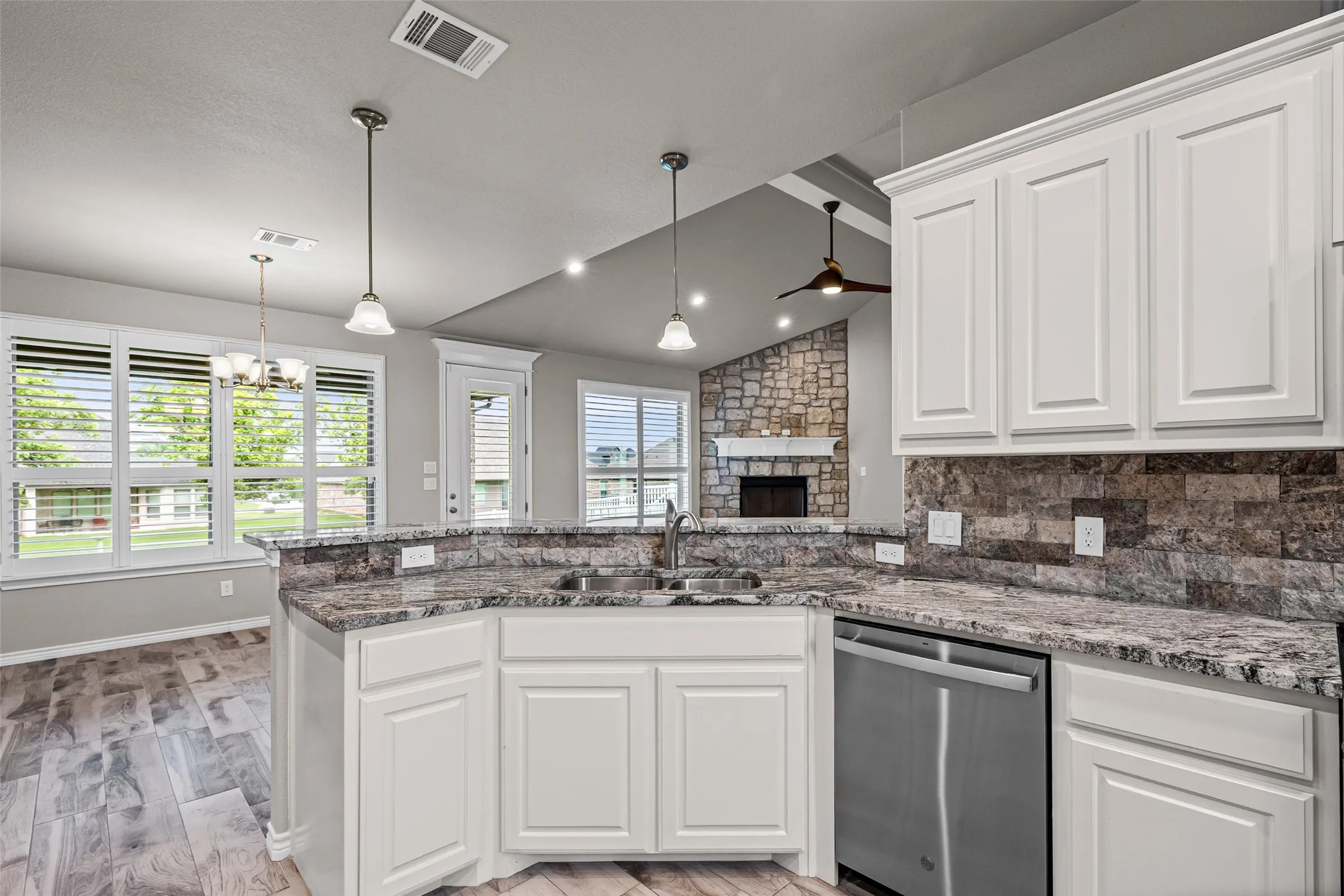 Kitchen featuring white cabinetry, granite countertops, an undermount sink, stainless steel dishwasher, and a stacked stone backsplash