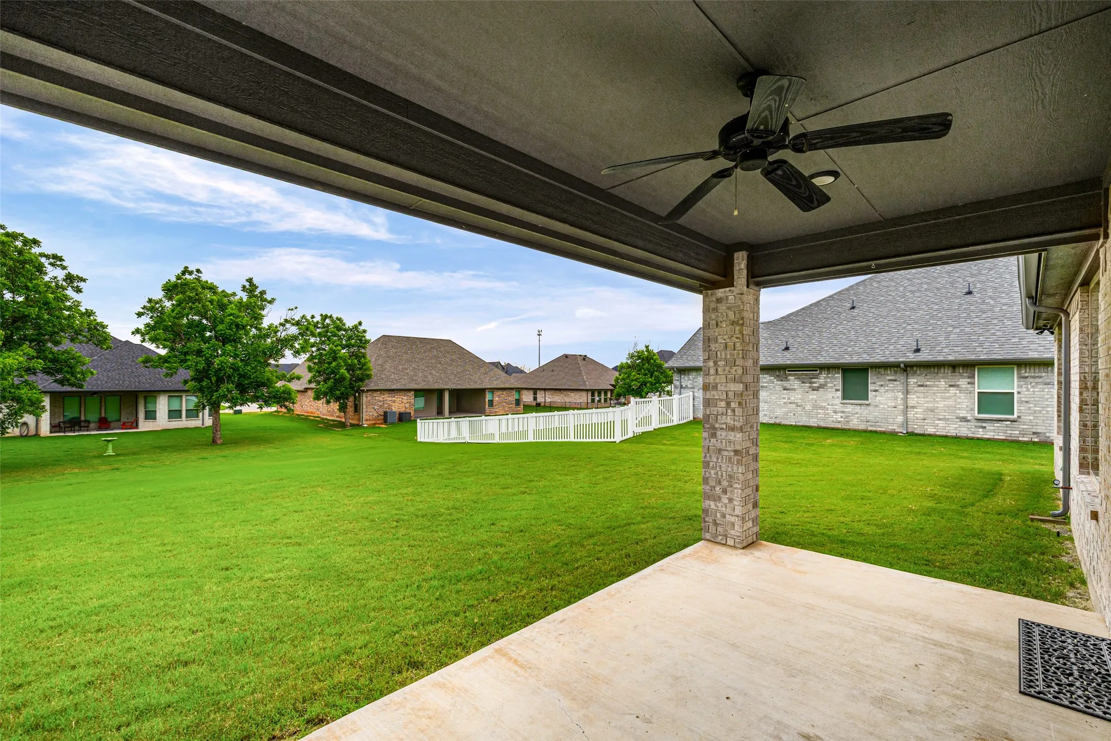 Covered patio featuring a ceiling fan with integrated lighting, brick support column, and concrete flooring