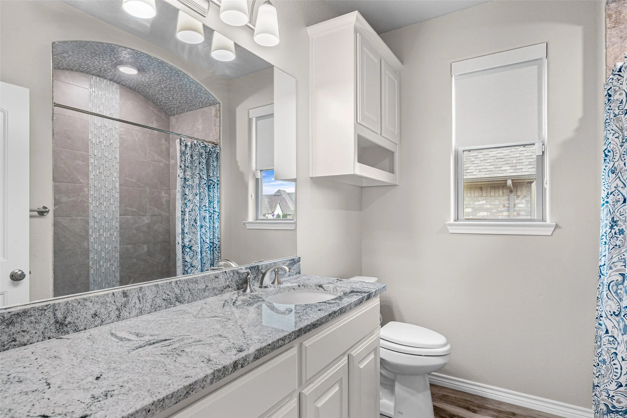 Full bathroom featuring a single vanity with stone countertop, white cabinetry, and wood-finish flooring