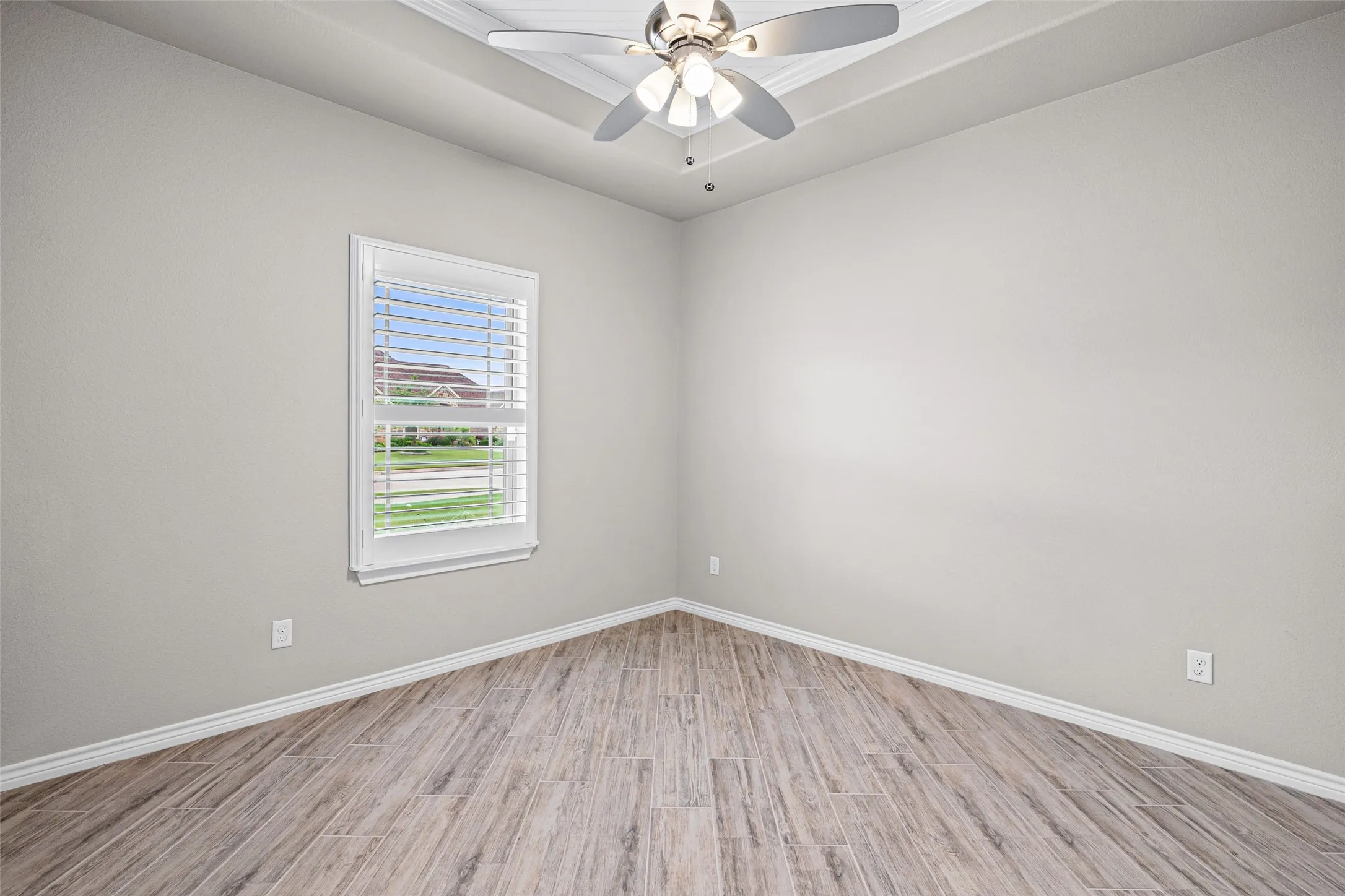 Neutral wall color with wood-finish flooring, a tray ceiling, and a ceiling fan with integrated lighting