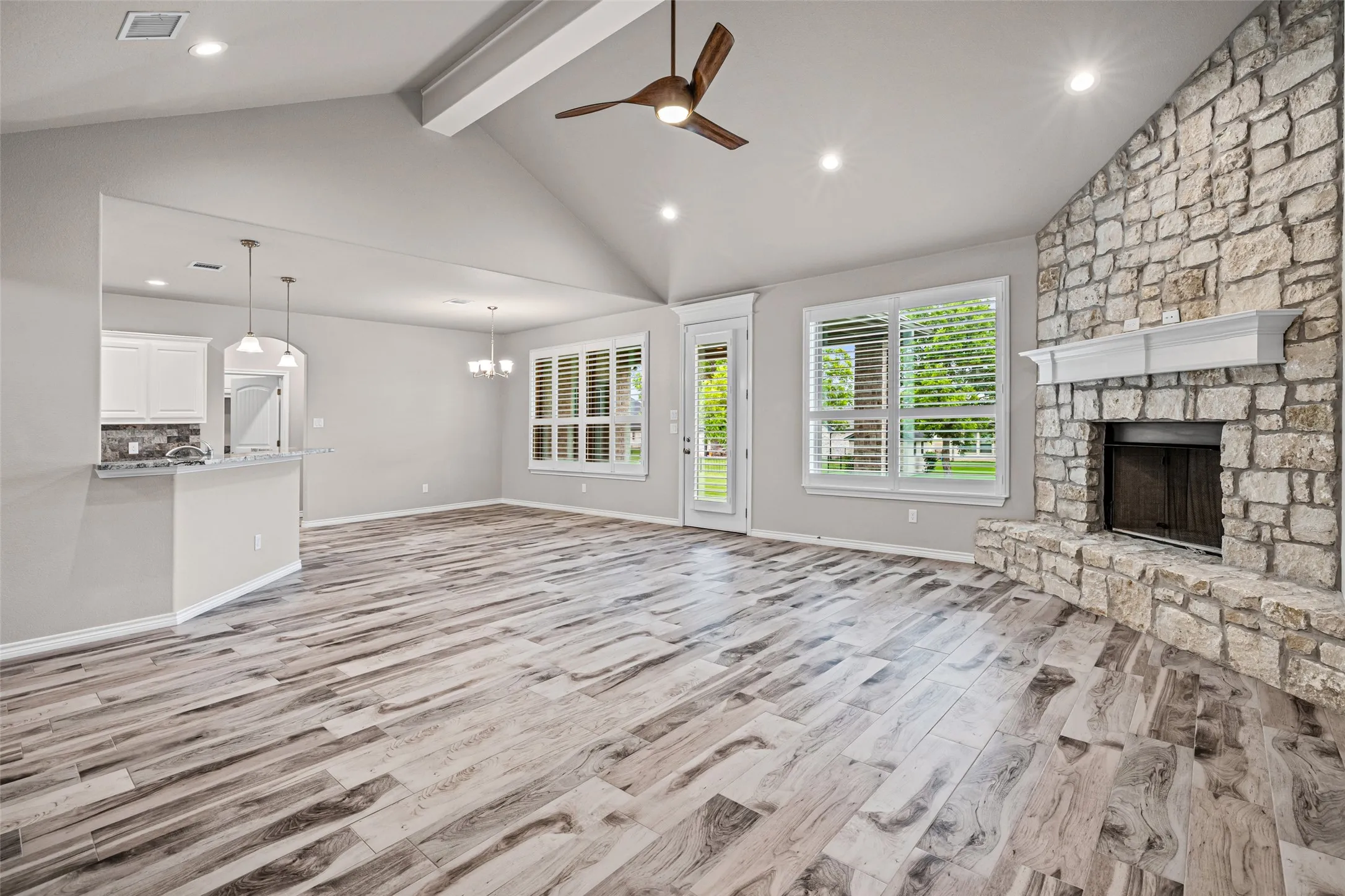 Spacious living area featuring a vaulted ceiling with exposed beam, a stone-clad fireplace with mantel, and wood-look​​‌​​​​‌​​‌‌​‌‌​​​‌‌​‌​‌​‌​​​‌​​ flooring