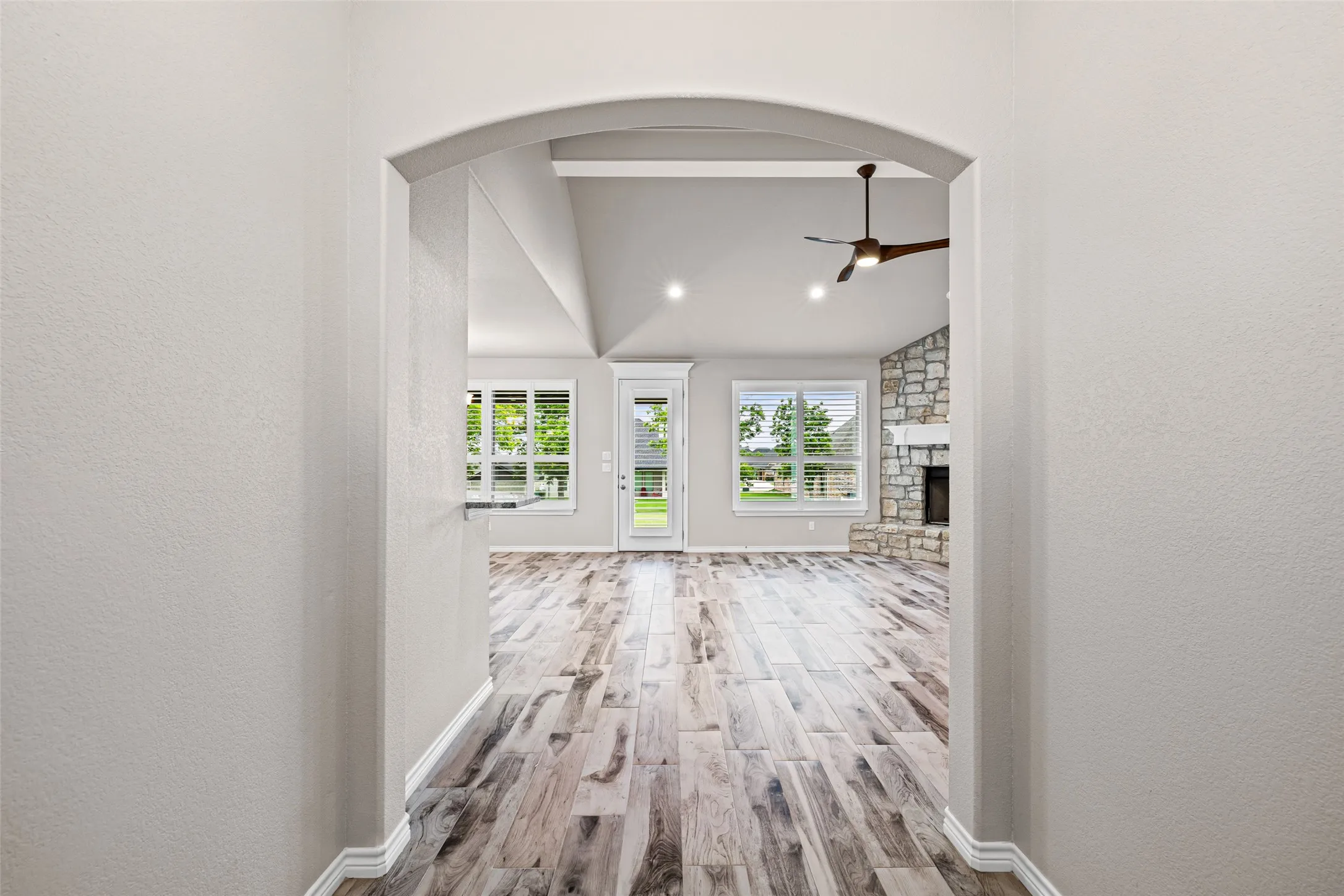 Archway entrance featuring wood-finish flooring, vaulted ceilings with a ceiling fan, and a stone-faced fireplace