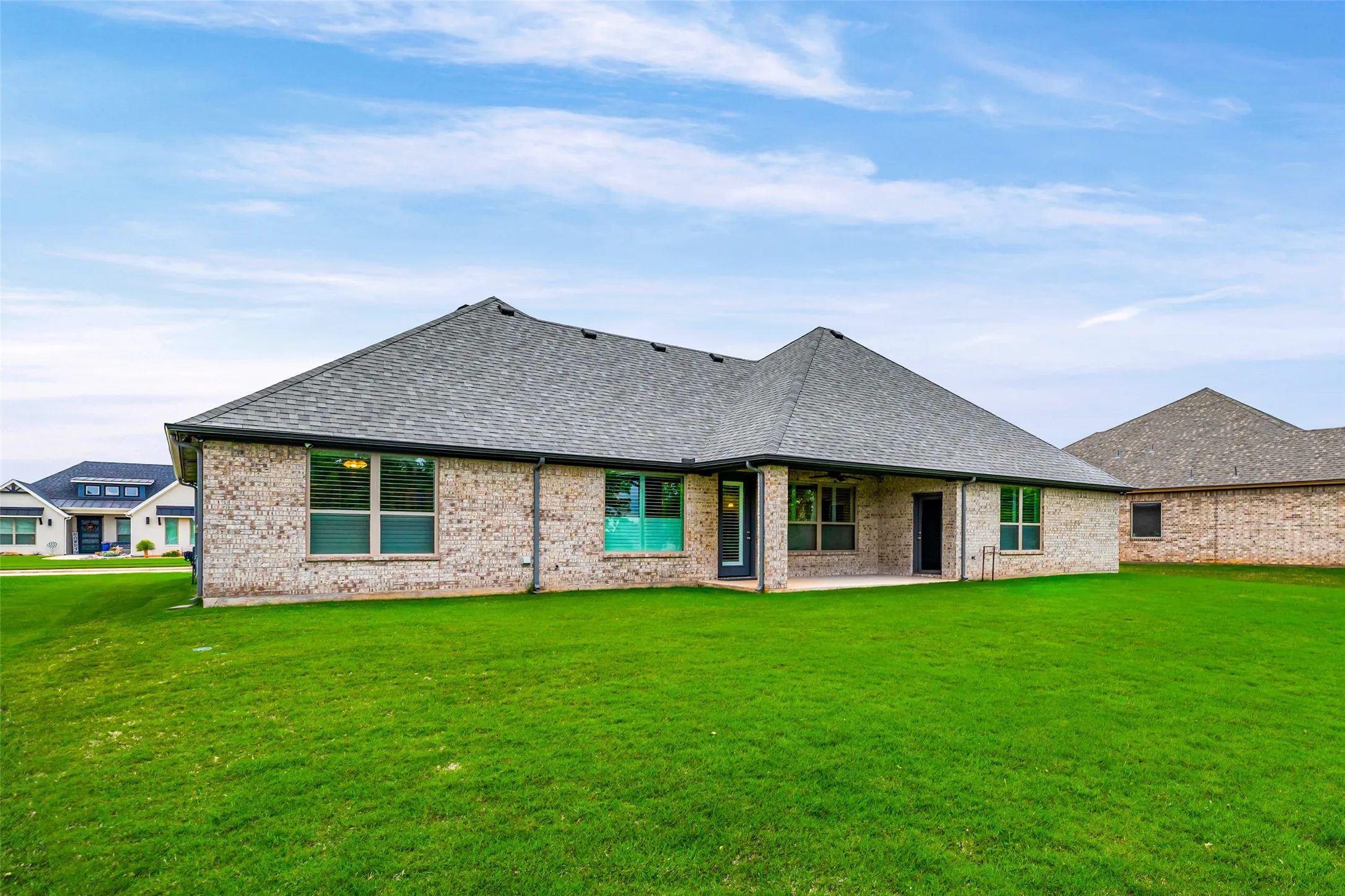 Expansive rear yard featuring a large green lawn, a brick exterior, and a covered patio area