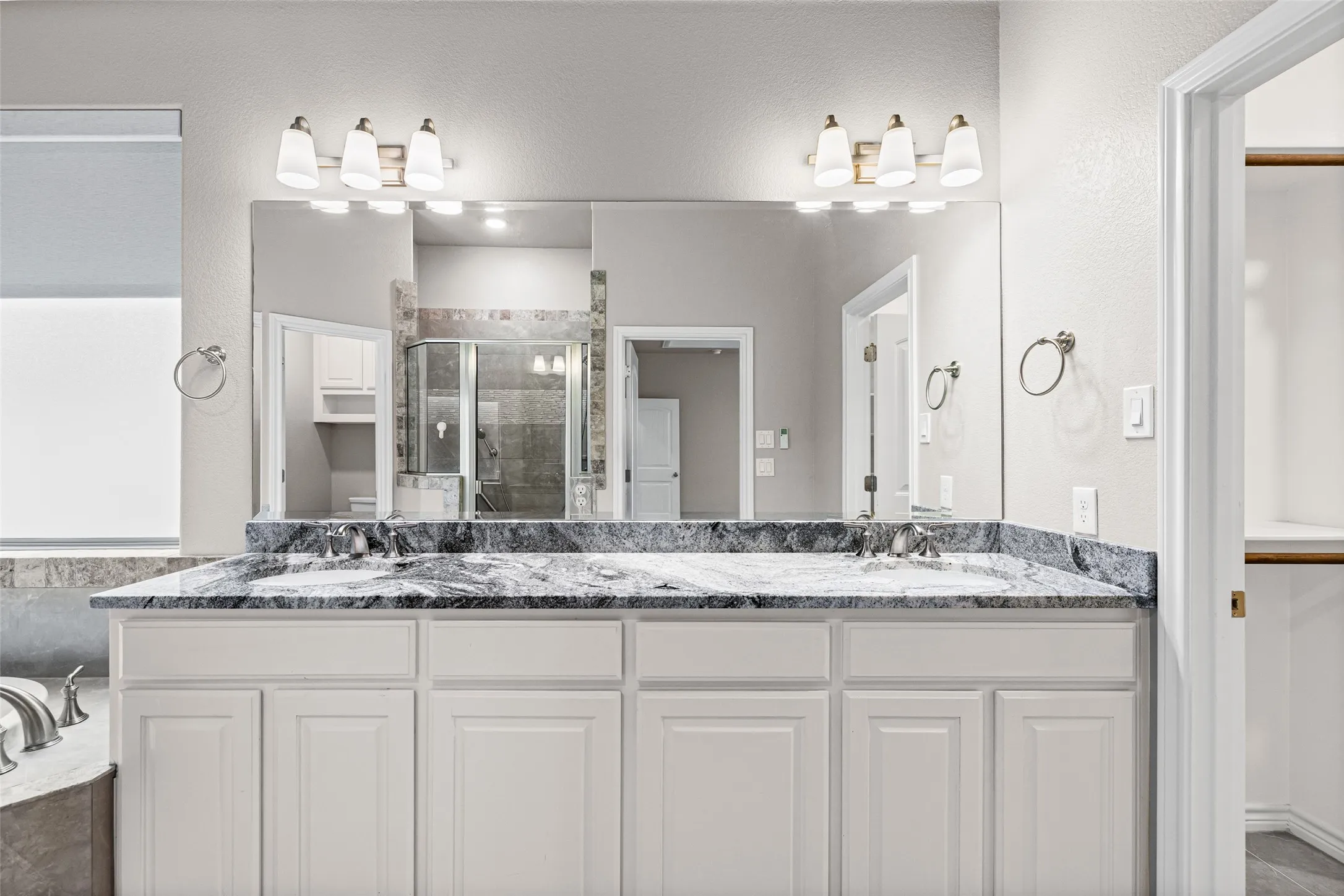 Double vanity featuring white cabinetry and a dark stone countertop