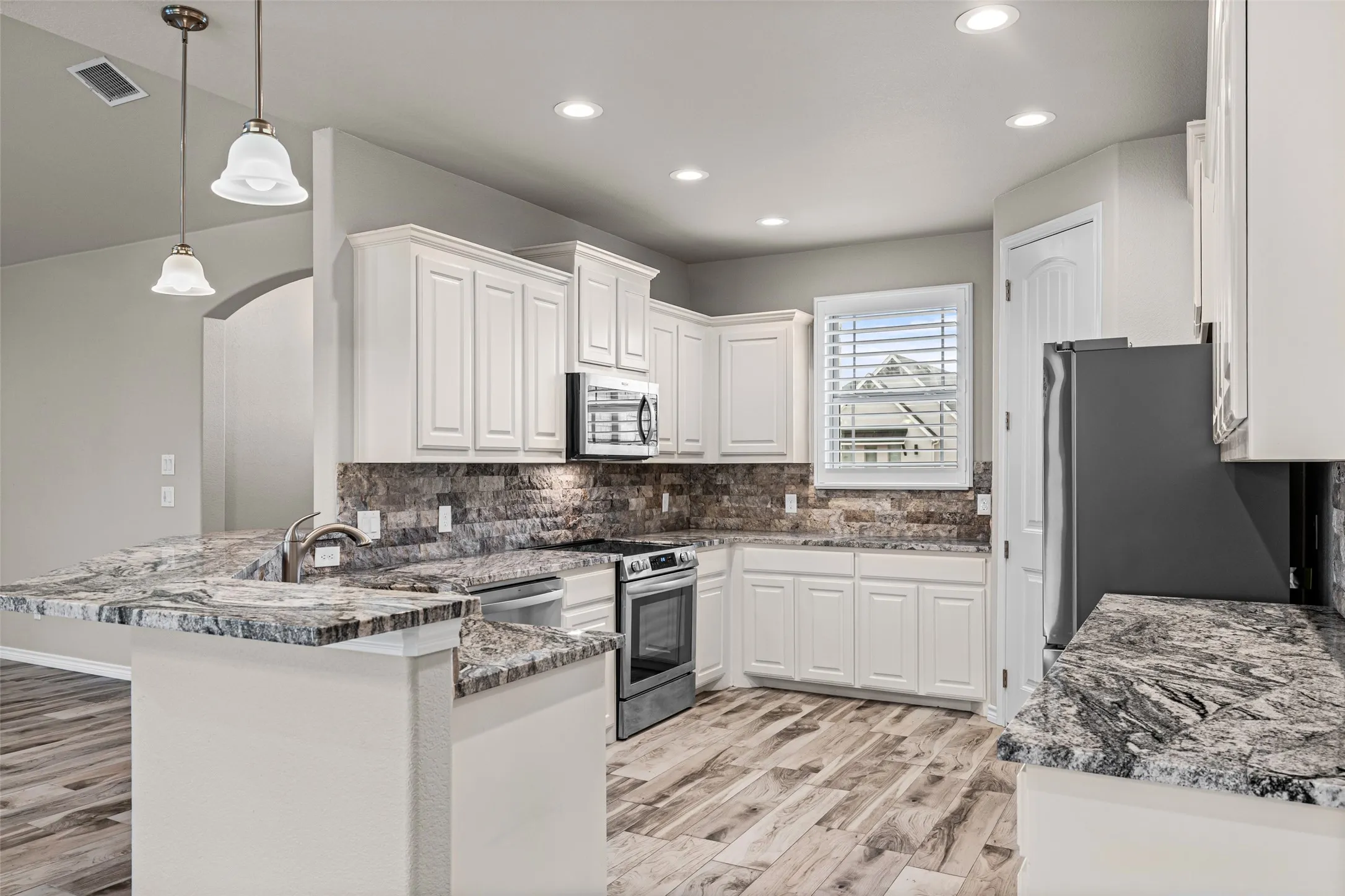 Kitchen featuring wood-finish flooring, white cabinetry, integrated stainless steel appliances, and multi-toned stone countertops