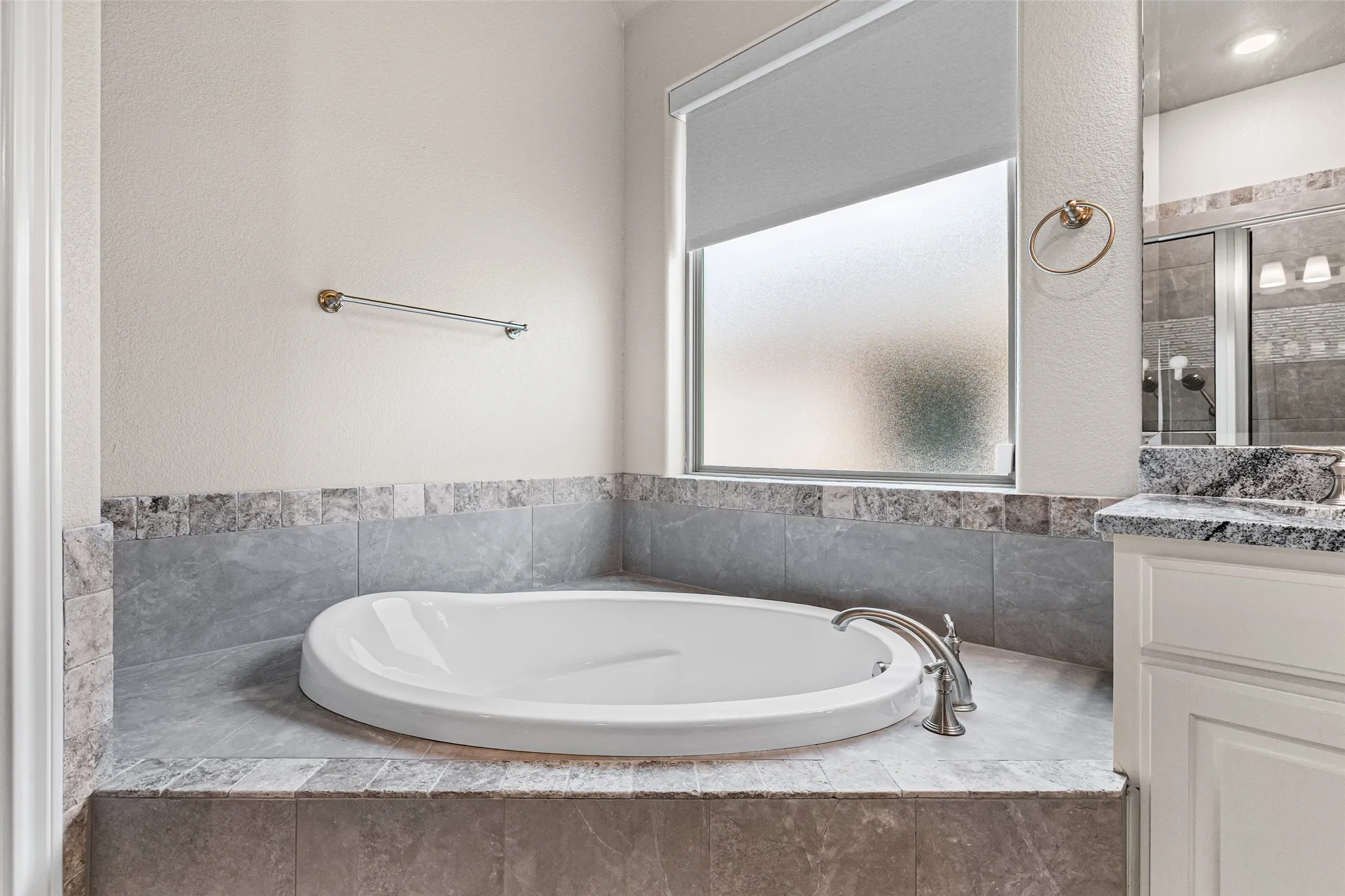Built-in soaking tub with brushed nickel fixtures, surrounded by grey-toned tile and a textured wall finish