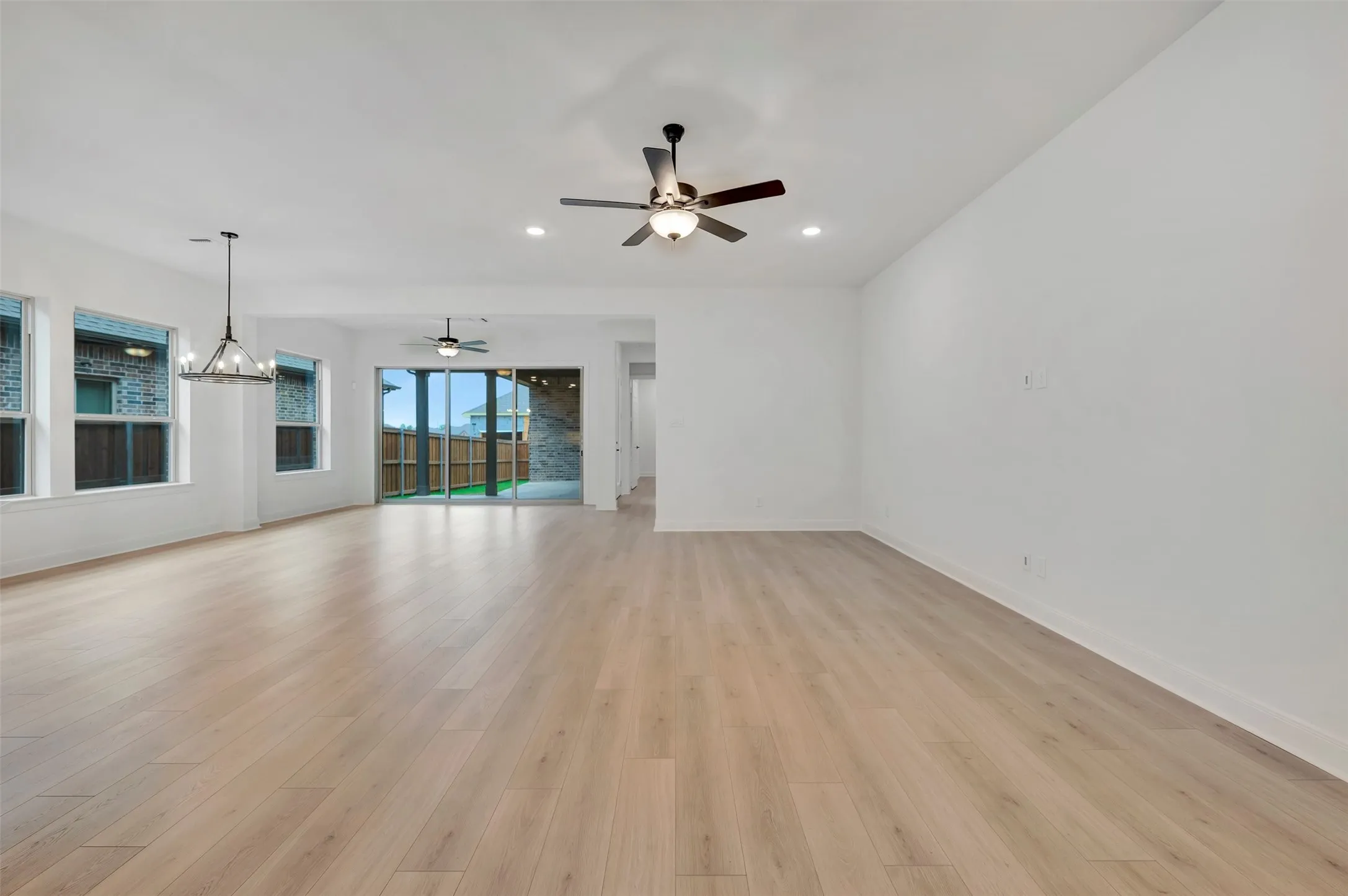 Expansive open-concept room featuring light wood-finish flooring, multiple windows, and a black chandelier