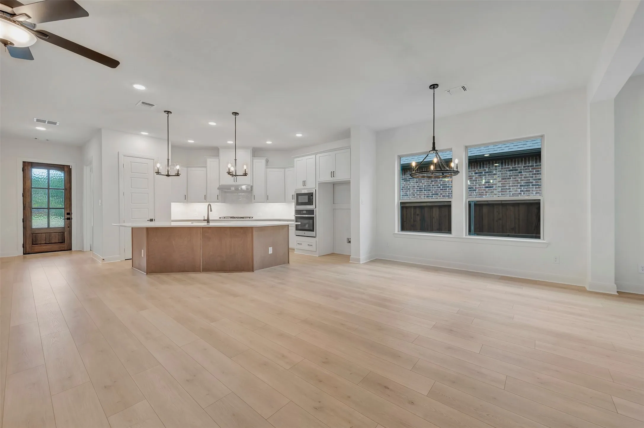 Open-concept living space featuring light wood-finish flooring, a kitchen island with a built-in sink, white cabinetry, and stainless steel double ovens