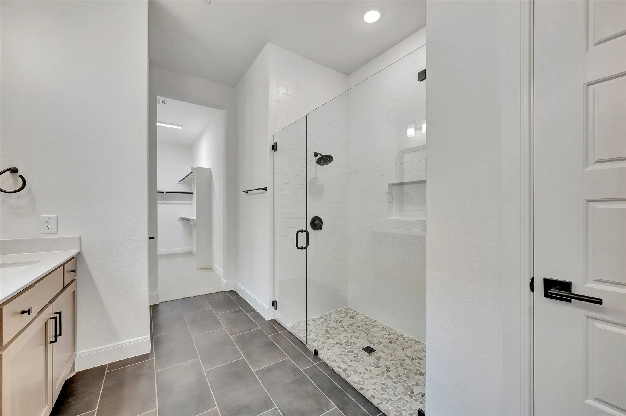 Tile-surround shower with a glass enclosure, pebble-style floor, and matte black fixtures