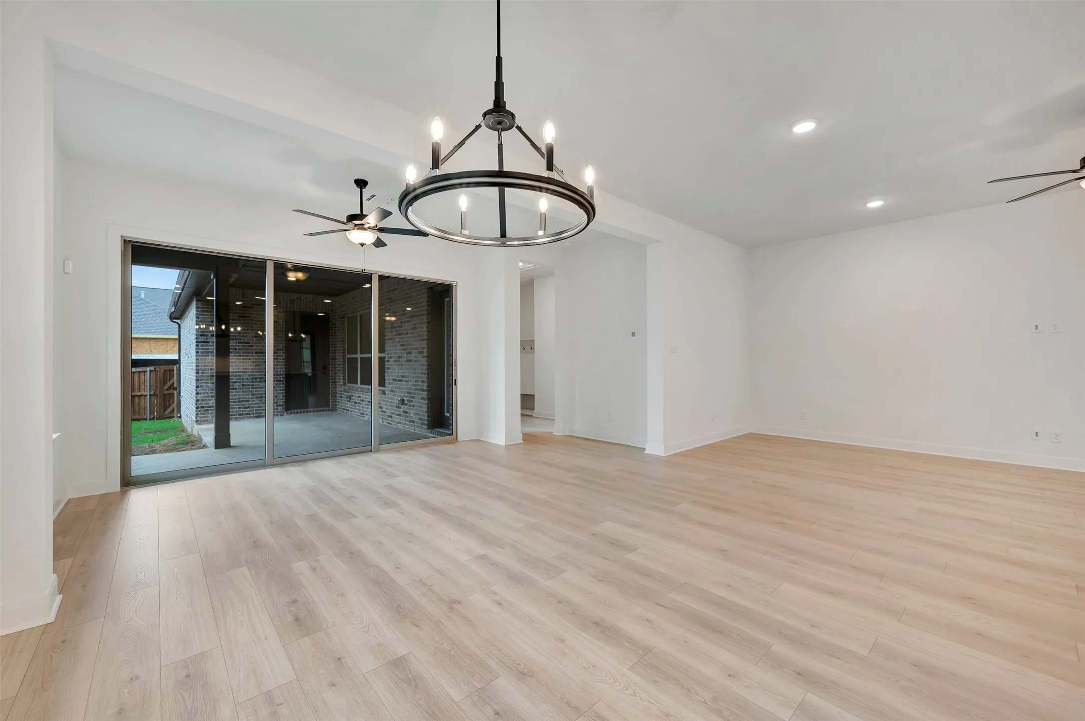 Spacious interior featuring light wood-finish flooring, a large sliding glass door, a contemporary chandelier, and recessed lighting