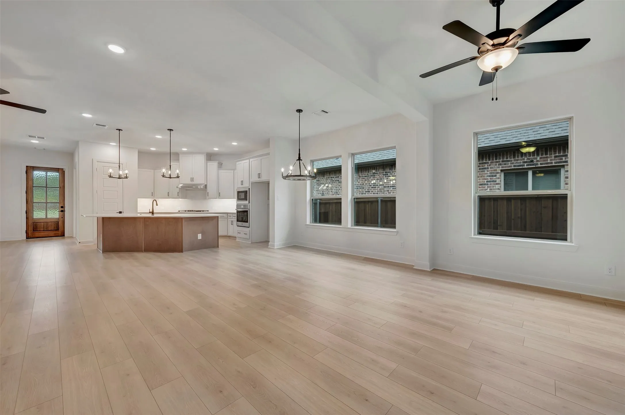 Expansive open-concept living area with light wood-finish flooring, recessed lighting, and a modern ceiling fan