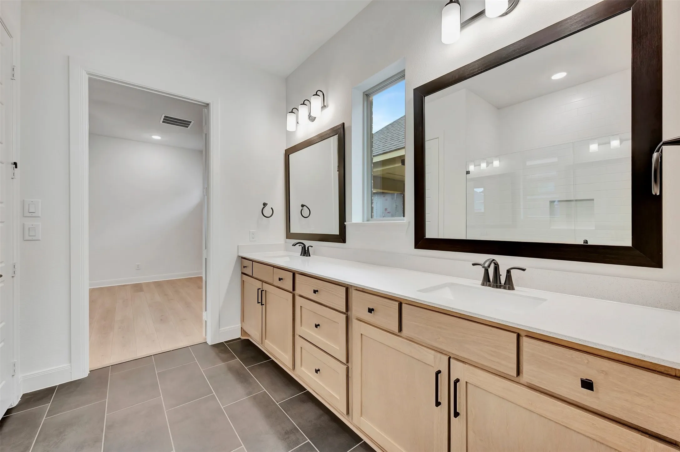 Dual vanity with light wood-finish cabinetry, white countertops, and dark framed mirrors