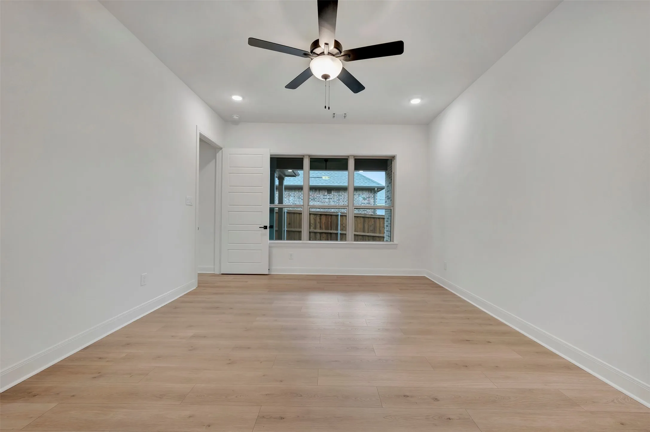 Light wood-finish flooring, recessed lighting, ceiling fan with integrated light, multiple windows, and a paneled door
