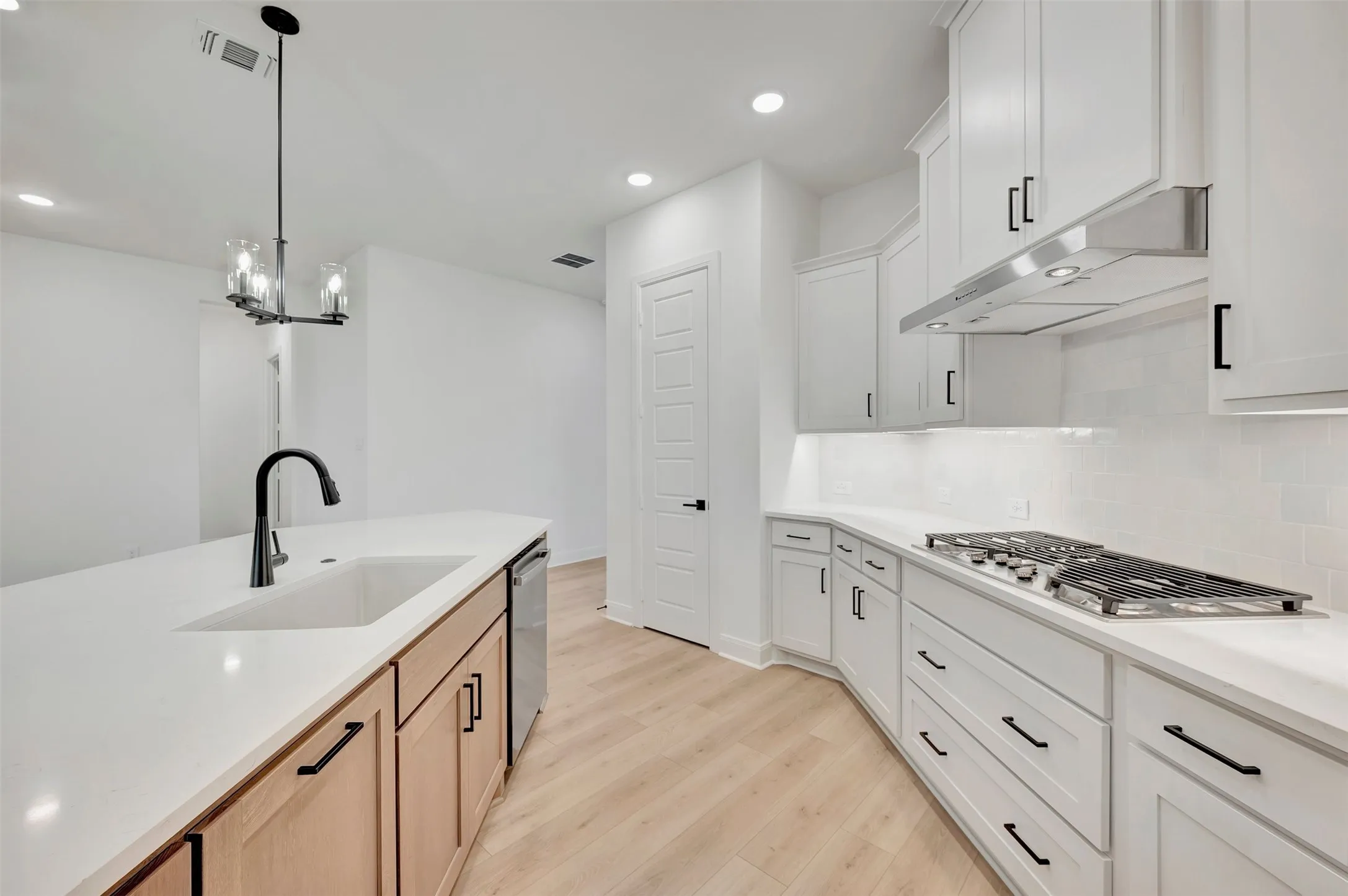 Kitchen featuring white cabinetry, light wood-finish flooring, a central island with a sink and black faucet, a stainless steel range hood, and a gas cooktop