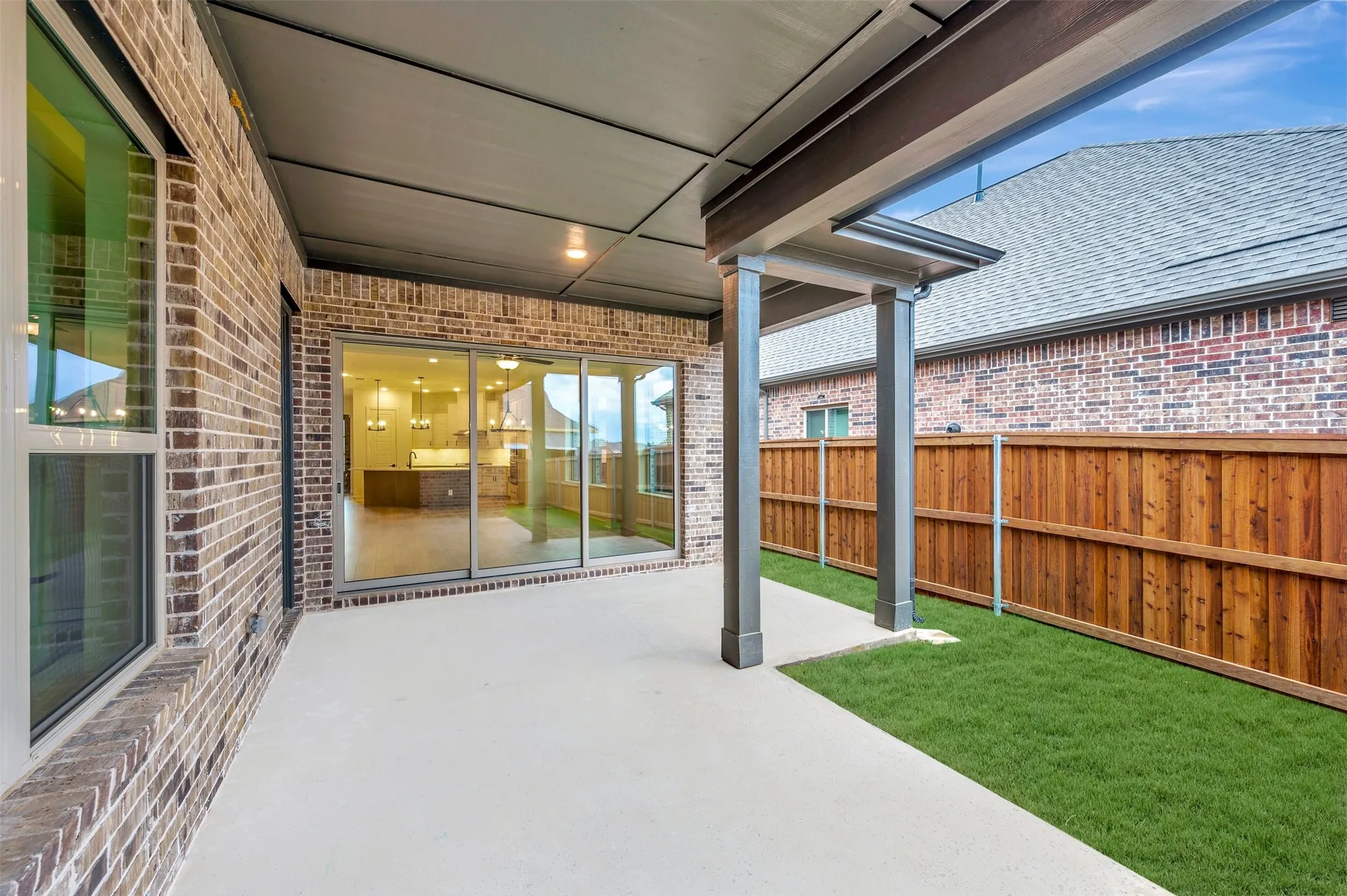 Covered patio with recessed lighting, brick exterior, sliding glass doors, wooden privacy fencing, and manicured lawn