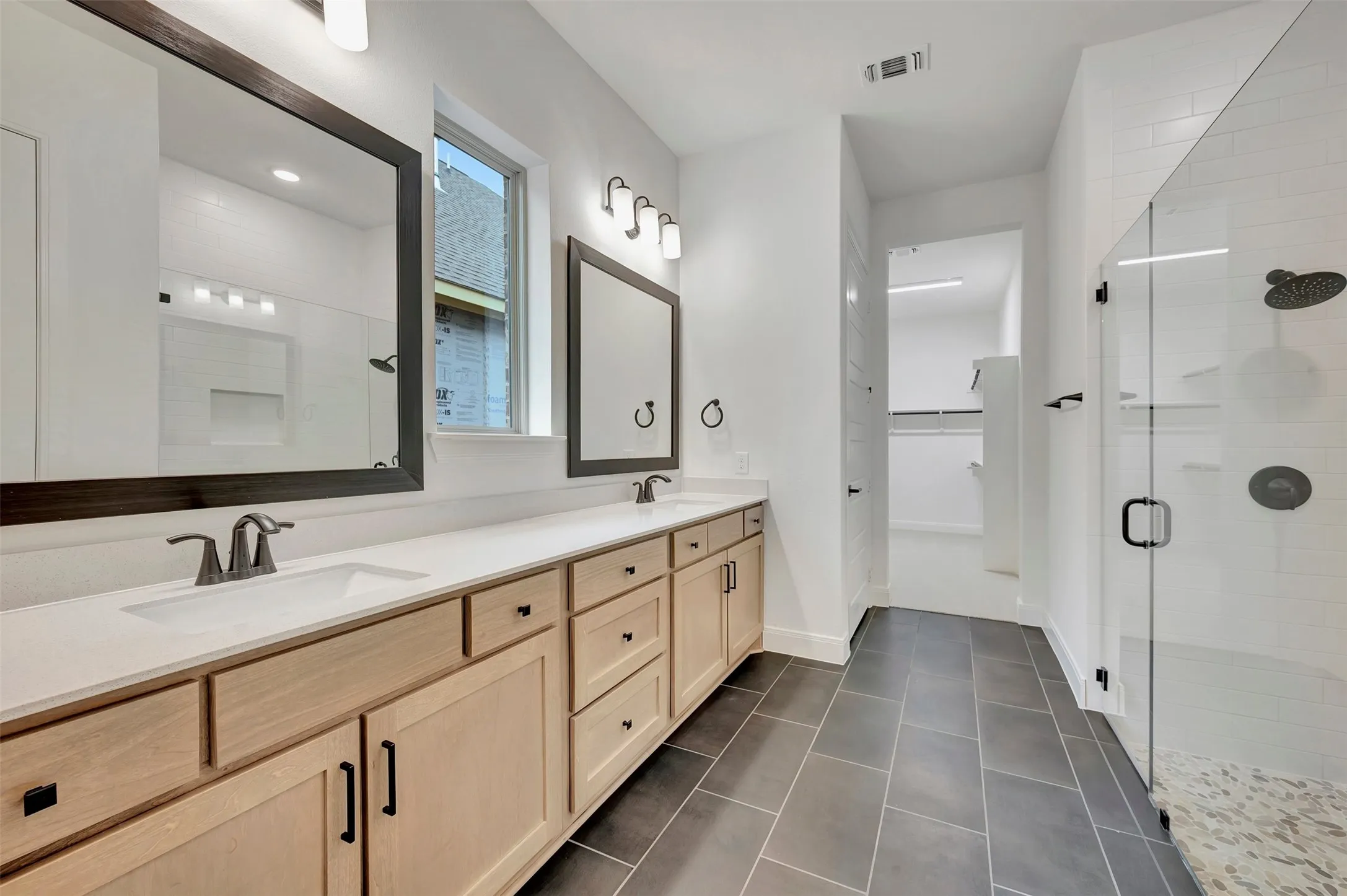 Dual vanity with light wood-finish cabinetry, white countertop, and dark framed mirrors