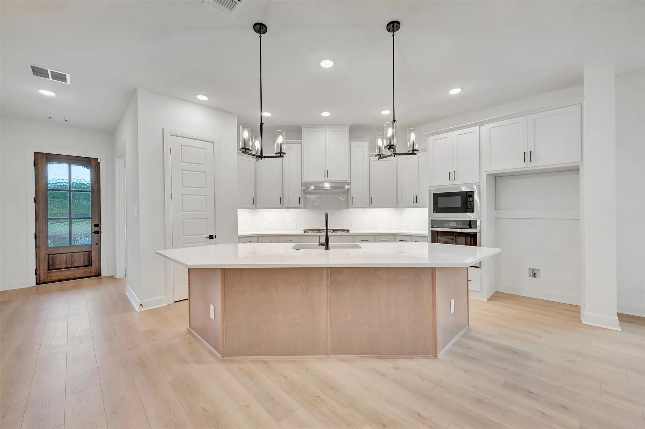 Kitchen with light wood-finish flooring, white cabinetry, integrated microwave, and a central island with a light countertop