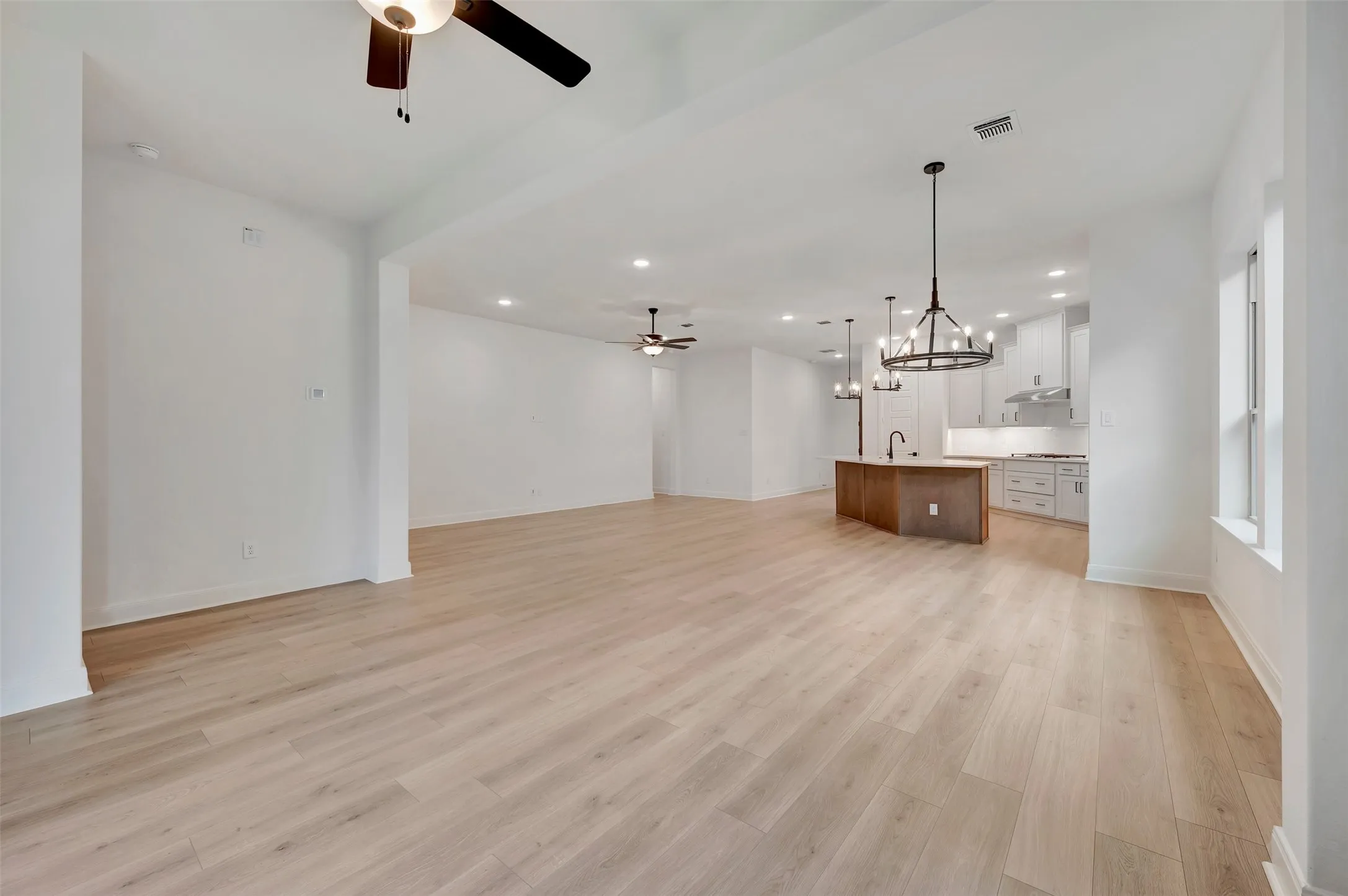 Expansive open-concept living space featuring light wood-finish flooring, recessed lighting, and ceiling fans