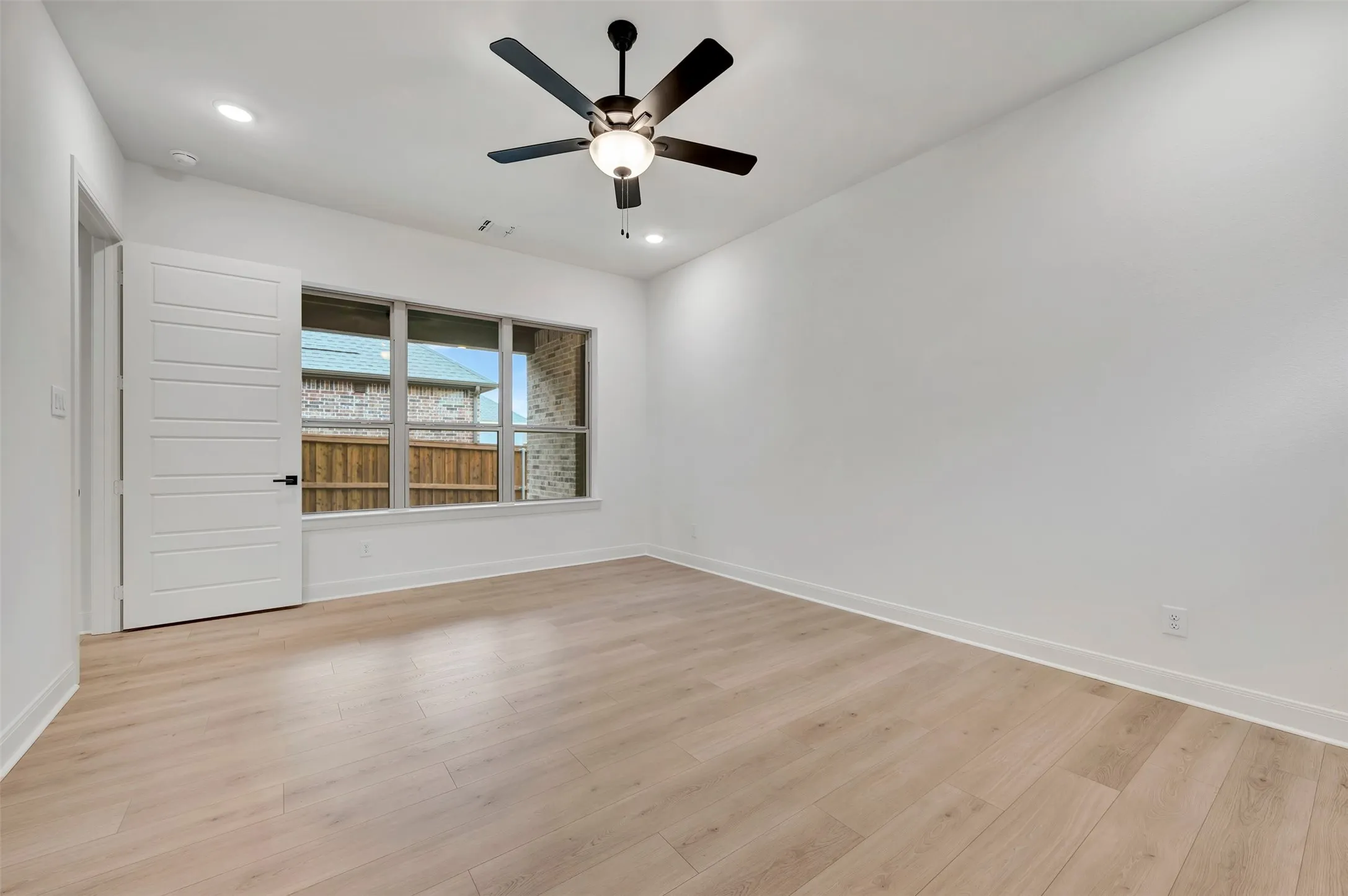 Wood-finish flooring, modern ceiling fan with integrated lighting, recessed lighting, white paneled door with dark hardware, and a horizontal window