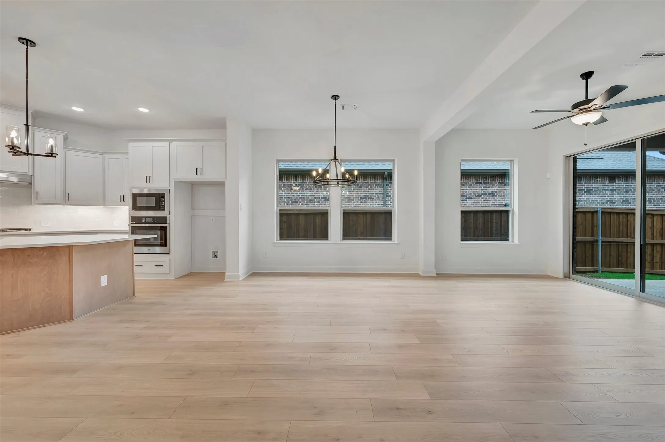 Open-concept living space featuring wood-finish flooring, white cabinetry, built-in stainless steel appliances, and a modern ceiling fan
