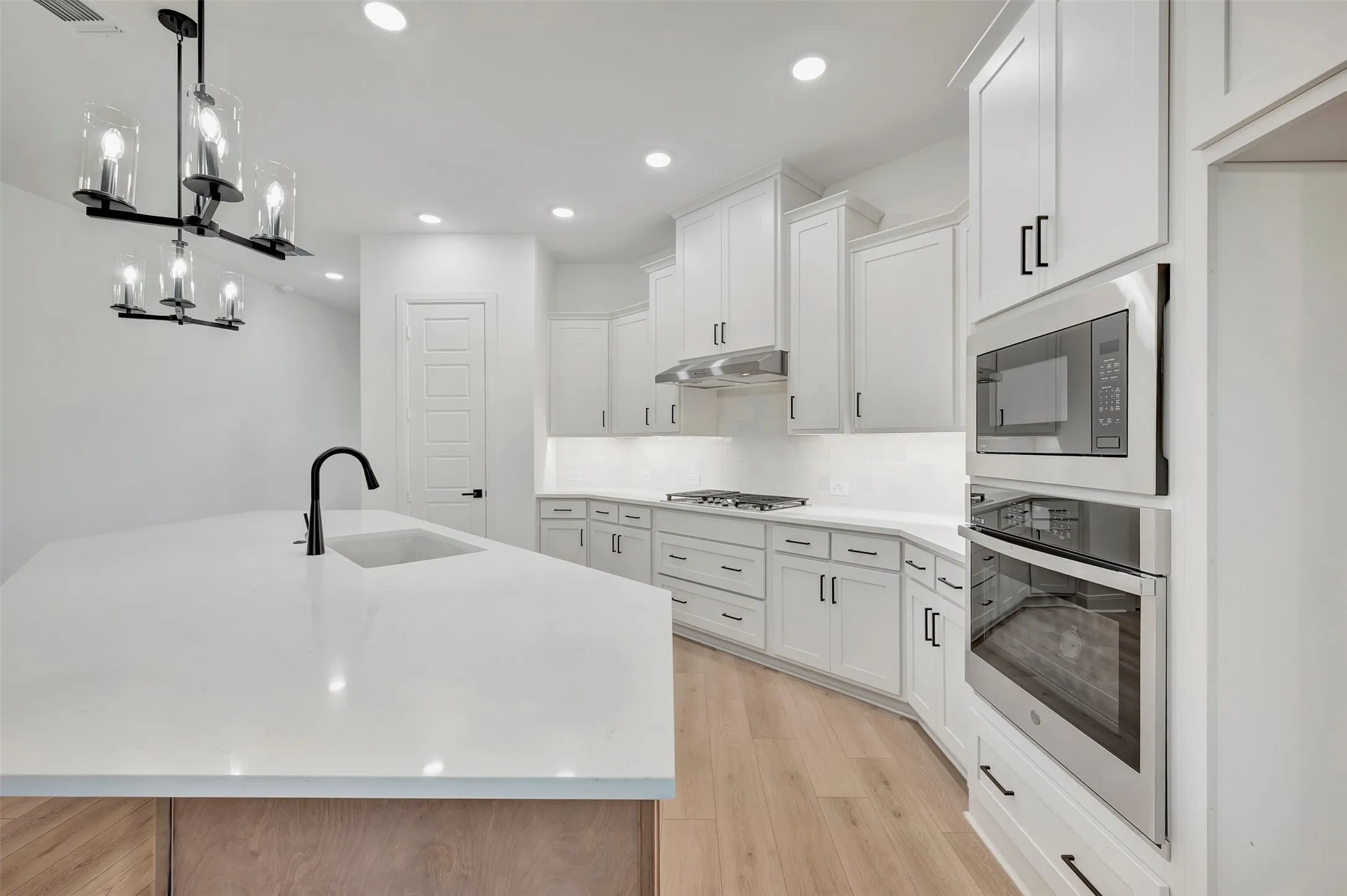 White cabinetry, wood-finish flooring, stainless steel appliances, recessed lighting, and a kitchen island with an integrated sink