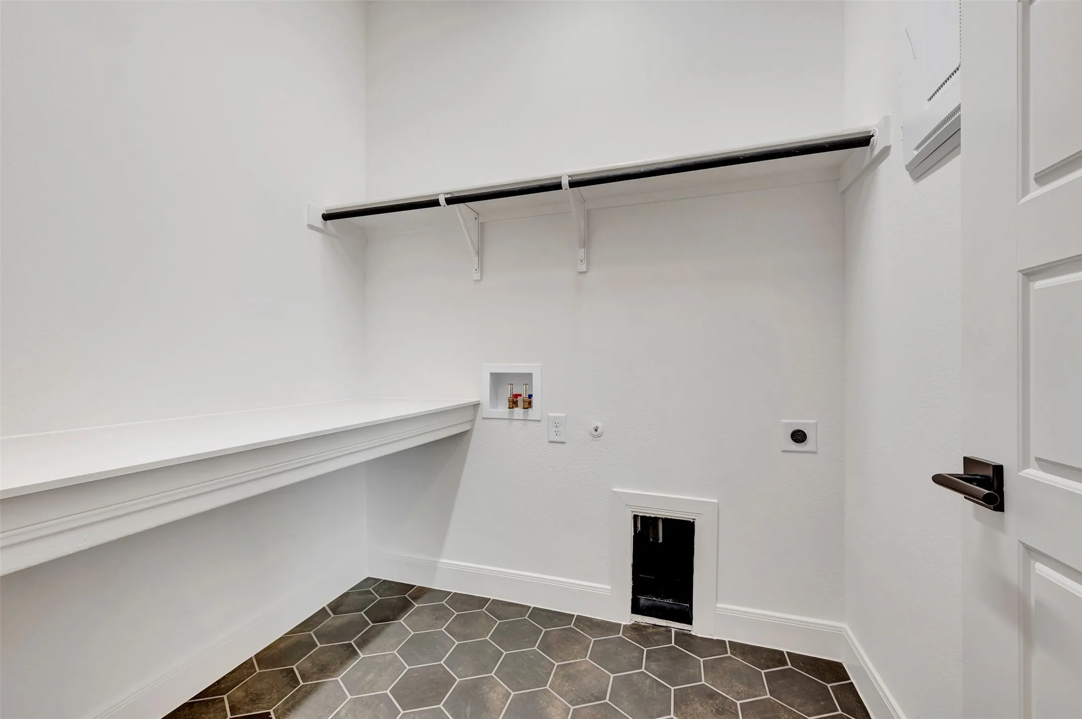 White walls, built-in shelving, dark hexagonal floor tiles, and a panel door with dark hardware