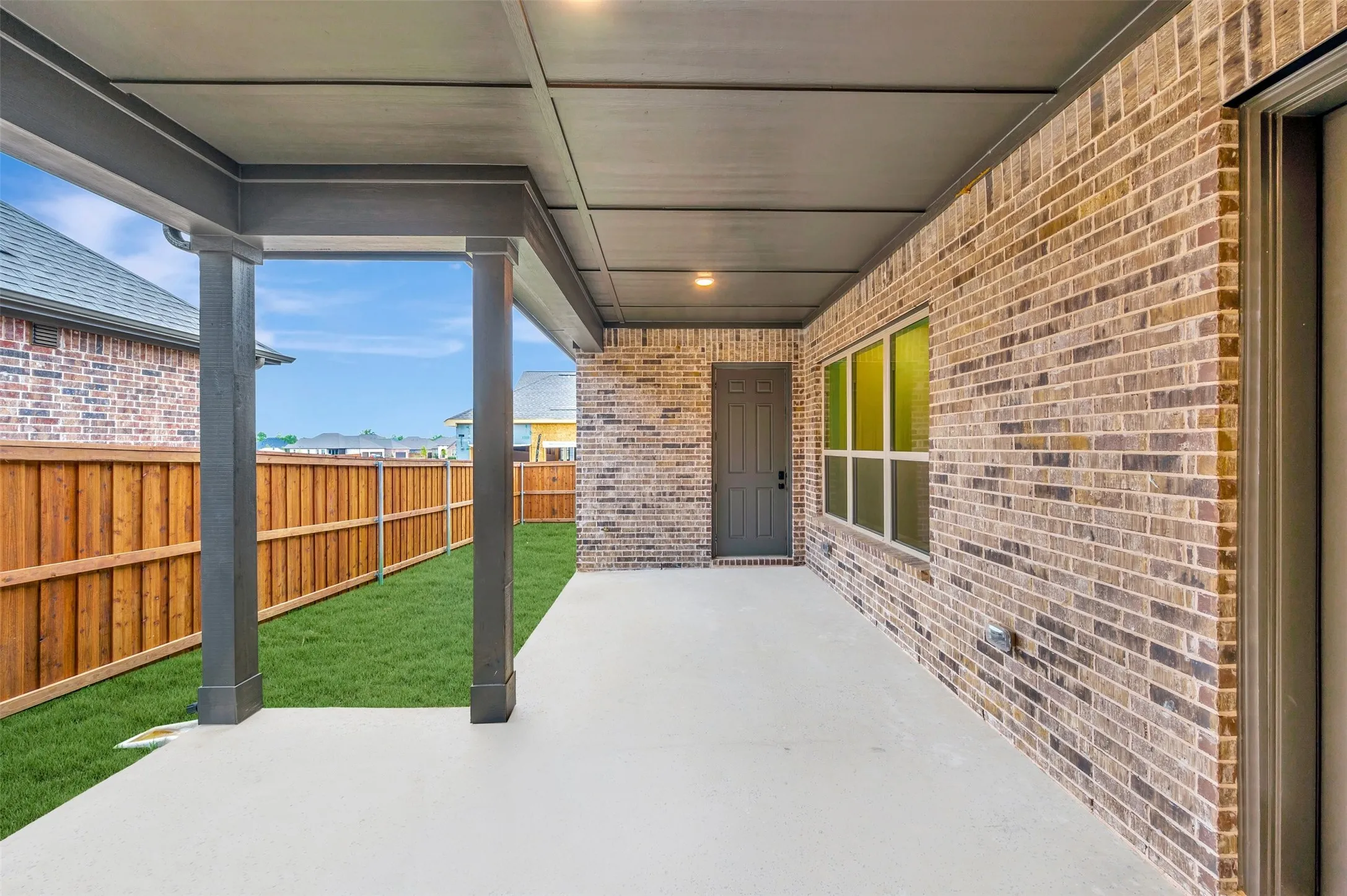 Covered concrete patio with recessed lighting, brick exterior, full backyard fencing, and an exterior door
