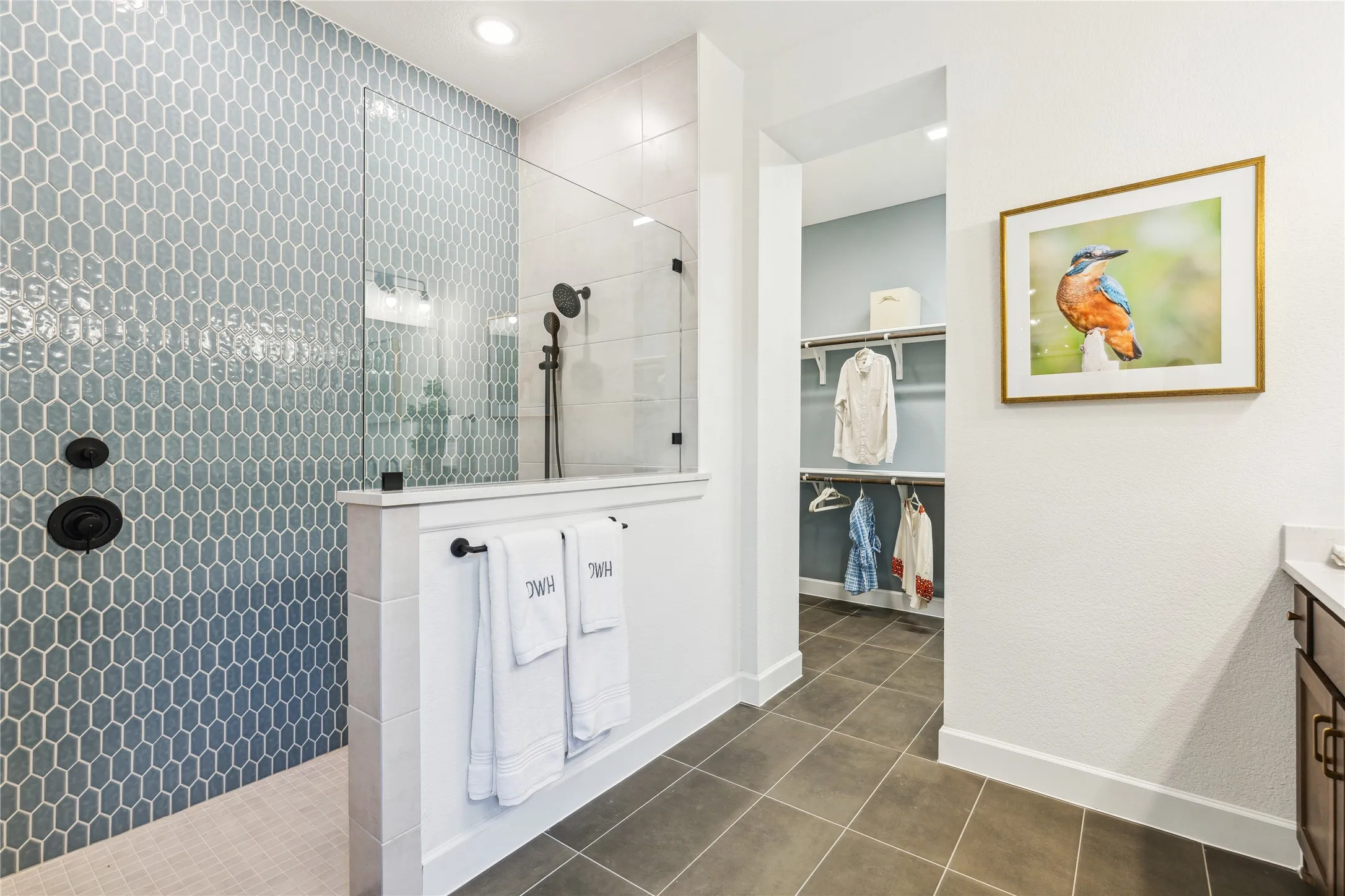 Spa-inspired primary bathroom featuring a walk-in shower with hexagonal tile surround and frameless glass enclosure, white shaker-style vanity with dual sinks, matte black hardware, and tile flooring