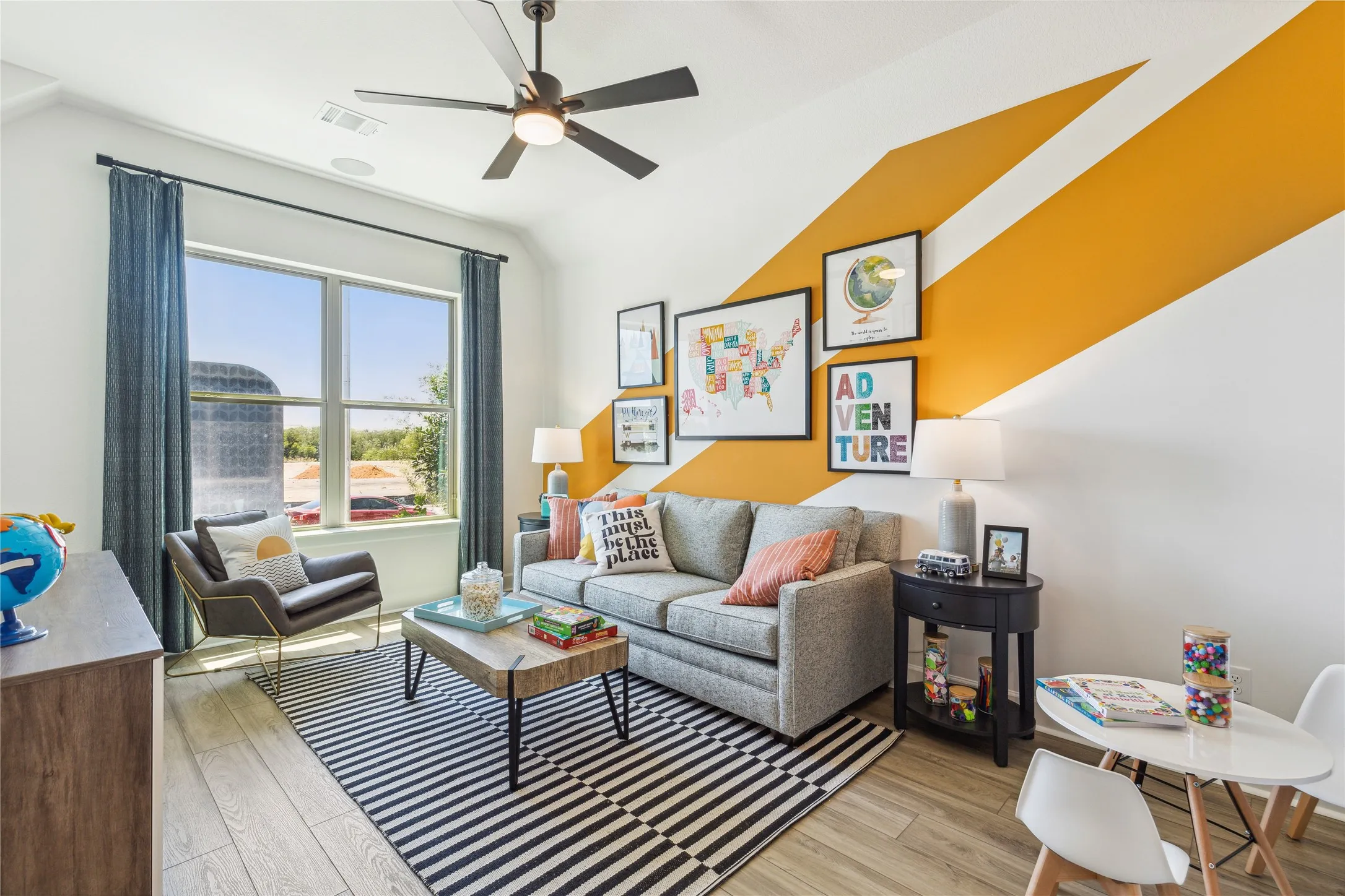 Bright, modern living room featuring floor-to-ceiling windows with natural light, ceiling fan, and wood-finish flooring