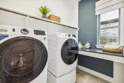 Modern laundry room featuring side-by-side front-load washer and dryer with large-capacity drums, digital controls, and sleek white cabinetry