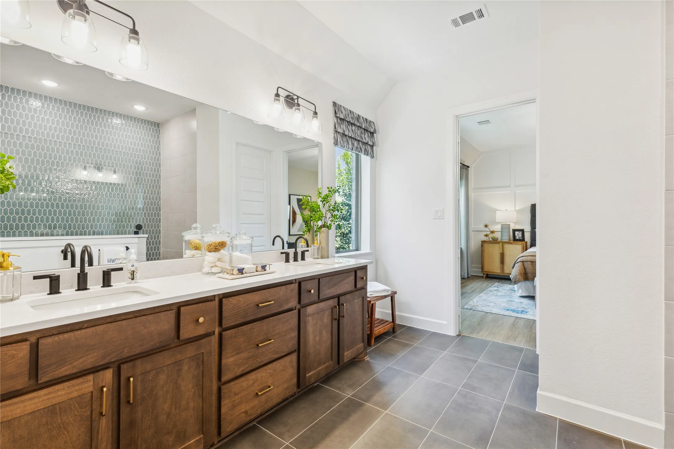 Spa-inspired primary bathroom featuring a lengthy wood-finish vanity with dual sinks, white quartz countertop, and matte black fixtures