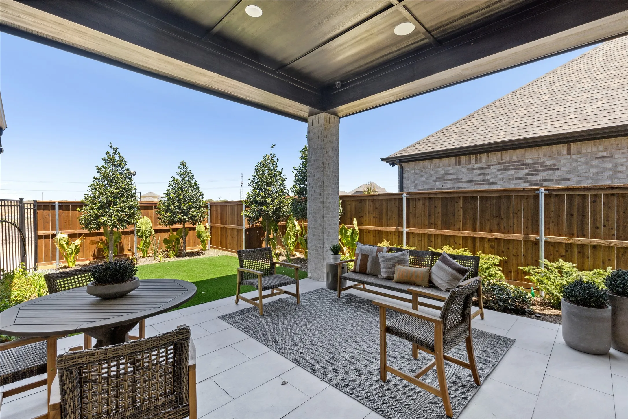 Expansive covered patio with concrete flooring and overhead beam structure, anchoring an entertainer's backyard