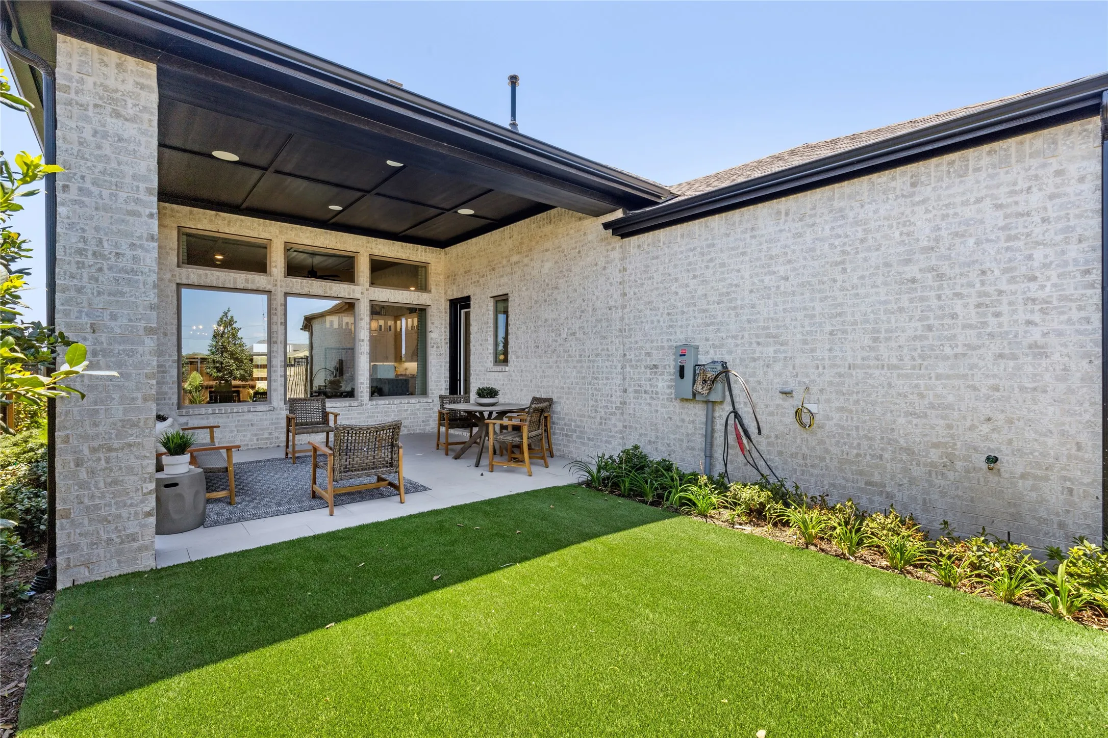 Expansive backyard oasis featuring a manicured lawn, covered patio with integrated lighting, and modern brick exterior