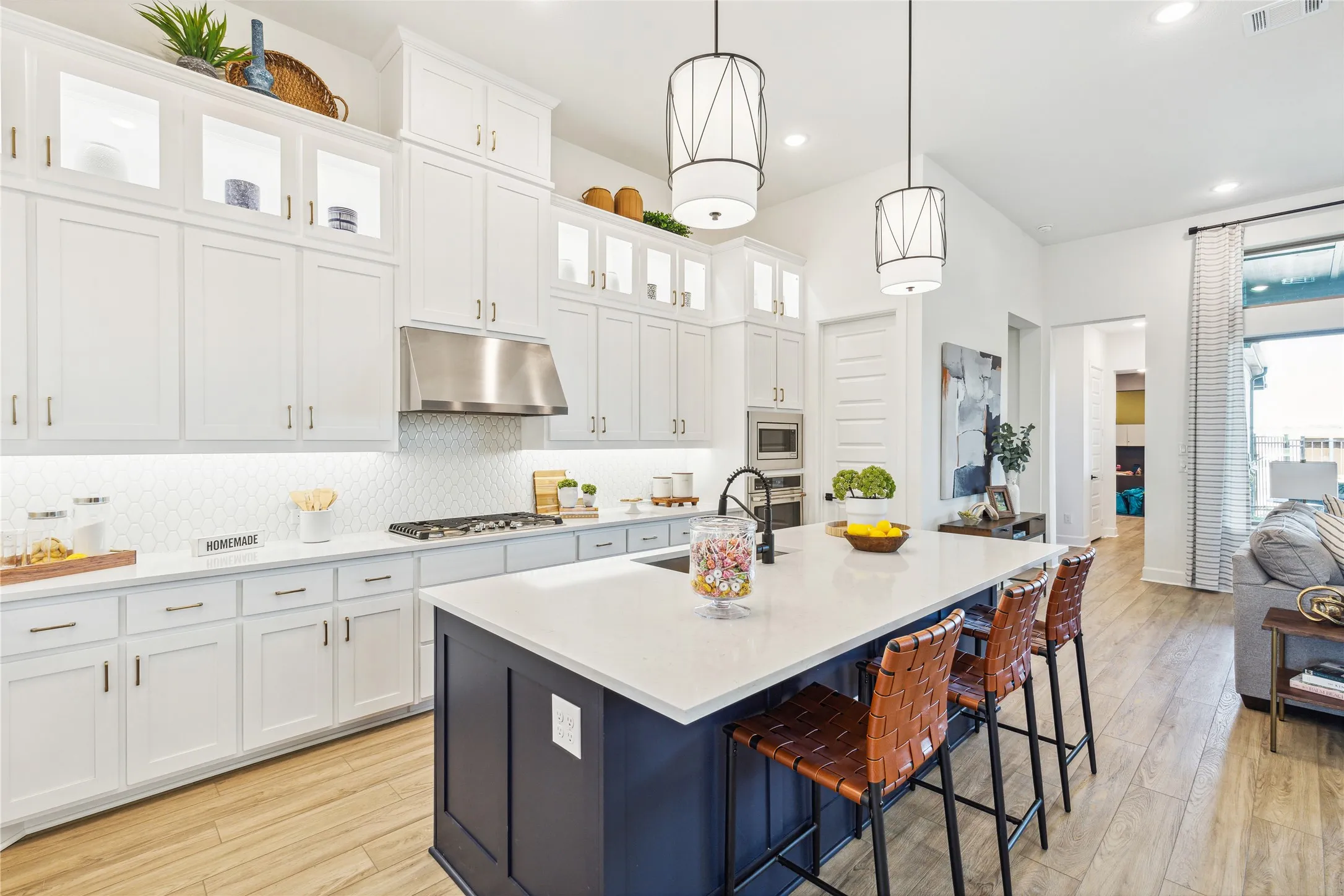 Chef's kitchen featuring white shaker cabinetry with abundant storage, stainless steel appliances including a gas cooktop, quartz countertops, and a striking navy island with seating for multiple guests