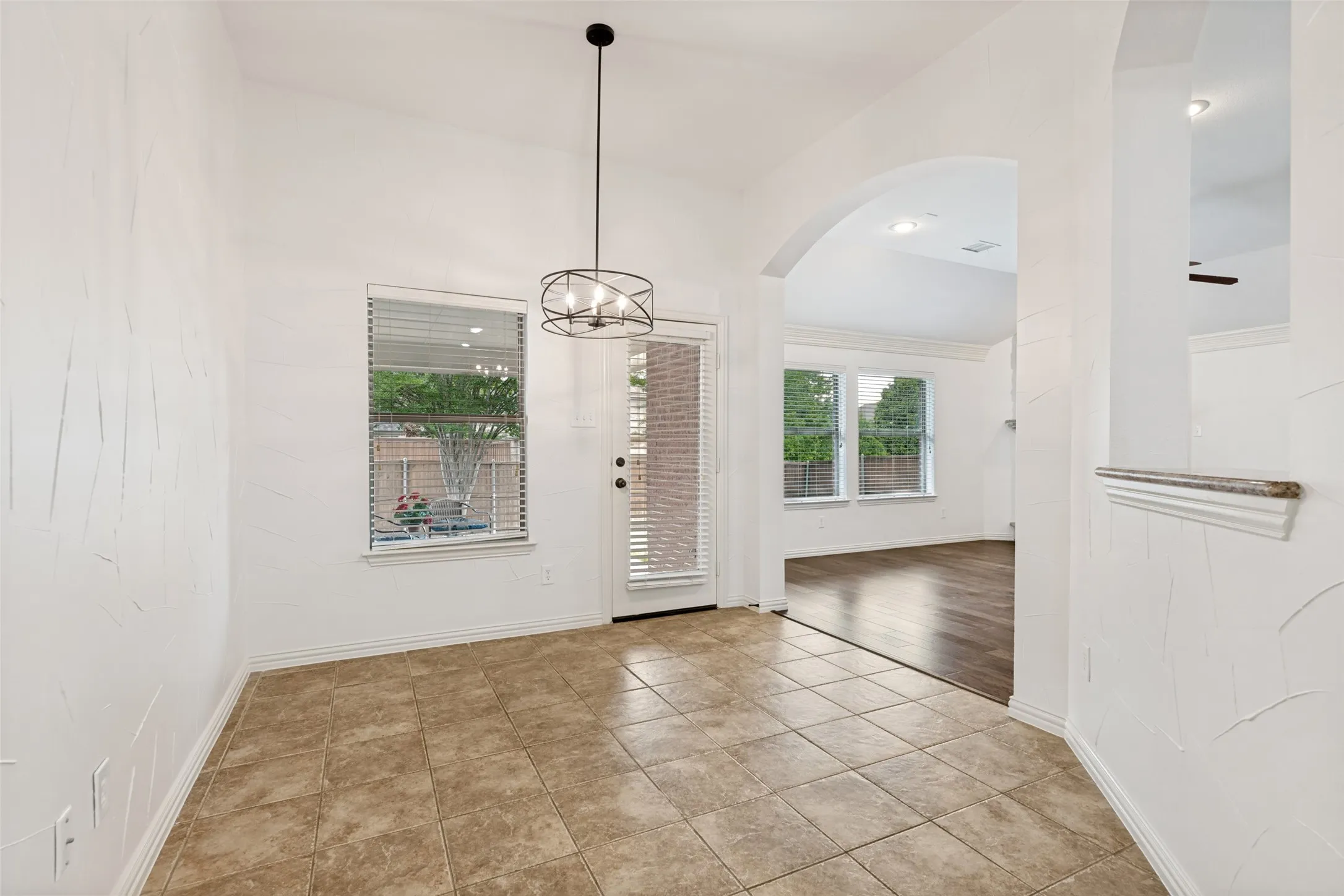 The light and bright Breakfast Room features tile flooring, a contemporary lighting fixture, and an arched entryway to the adjacent family room.