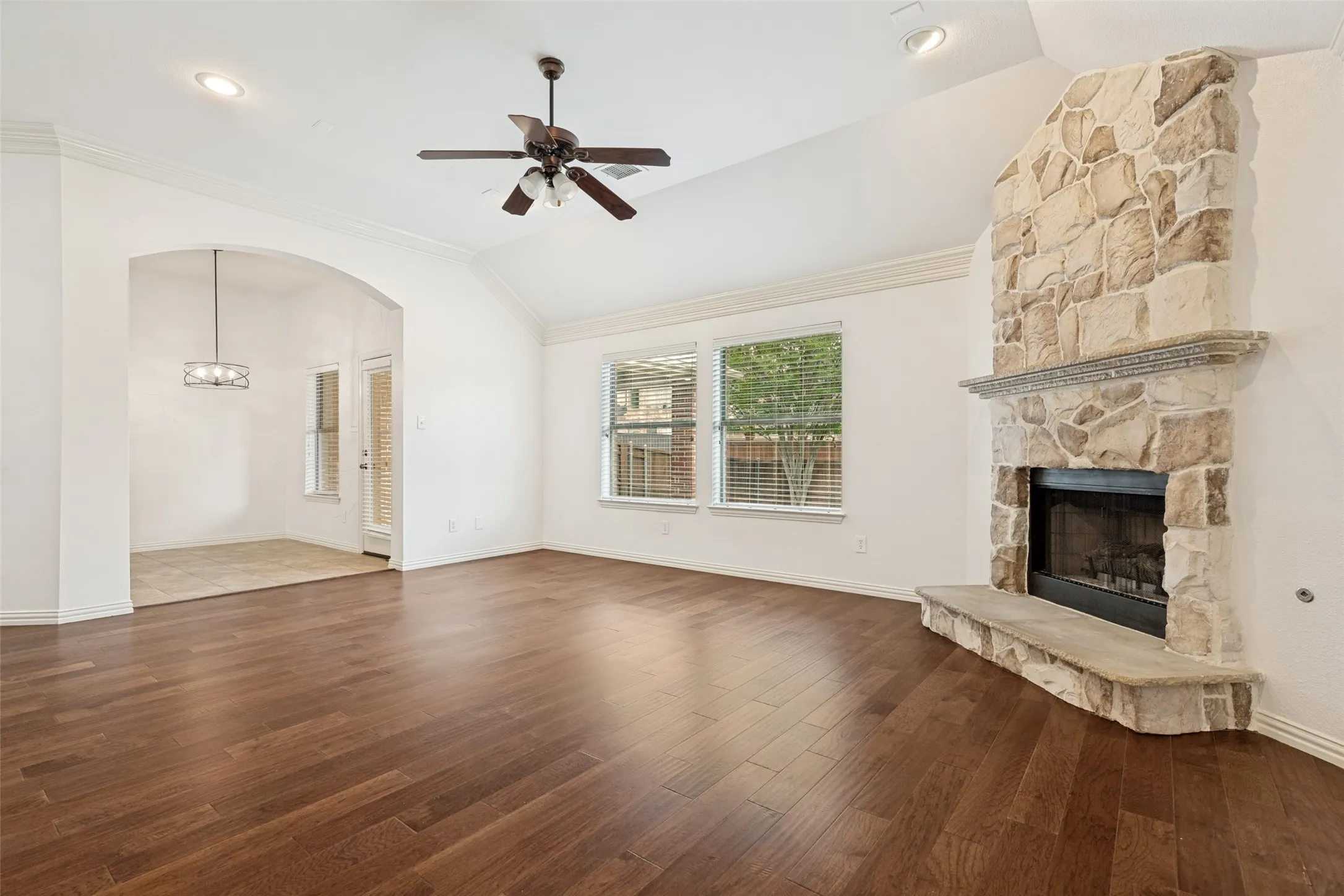 Another view of the family room featuring engineered wood flooring, a vaulted ceiling, and a stone fireplace with gas logs, a hearth, and views of the backyard.
