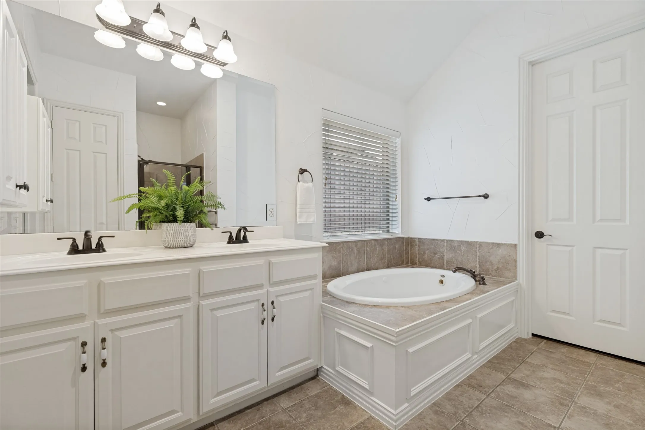 The Primary Bathroom featuring a dual vanity with white cabinetry, medicine cabinet, a large built-in mirror, and a jetted tub with tiled surround + large walk in closet.