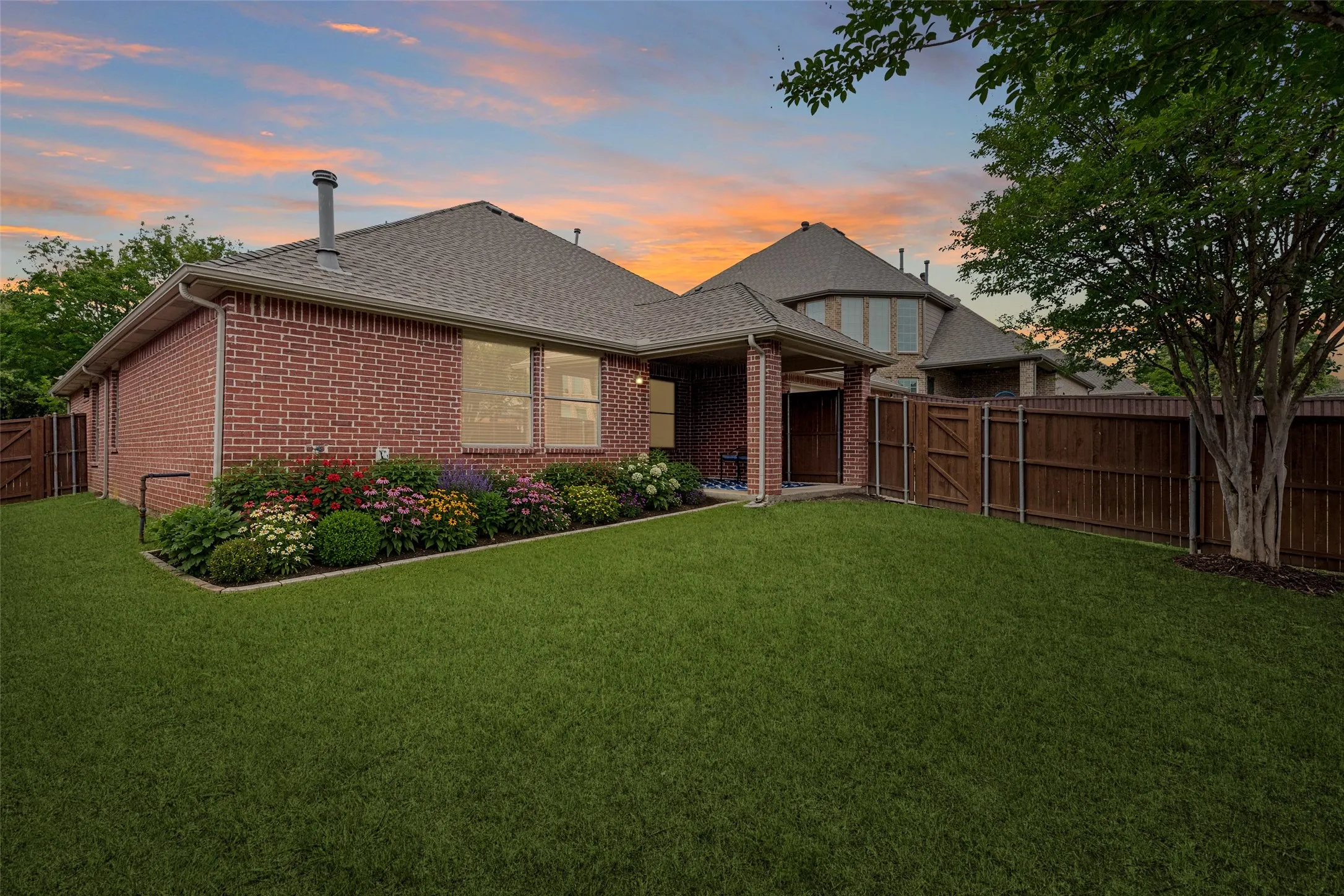 Expansive lawn with crepe myrtles, stone edge flower bed and covered patio.