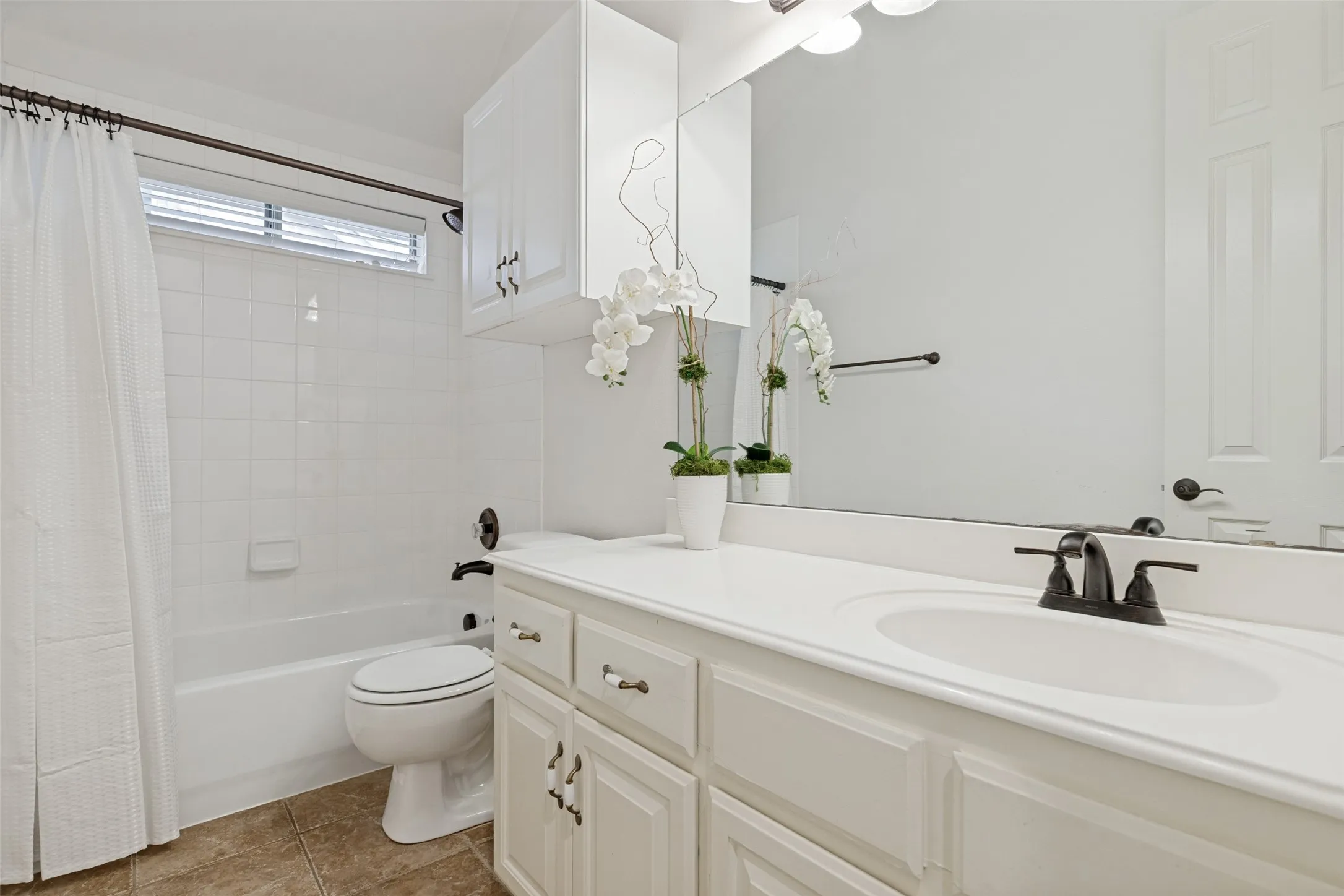 Bathroom featuring a white vanity with an integrated sink, recent dark bronze fixtures, storage cabinet and a white tile shower surround.