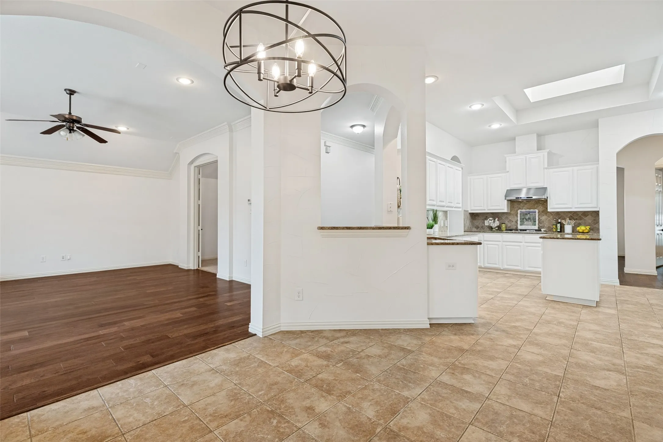 Open-concept living area featuring a kitchen with white cabinetry, stainless steel appliances, and a tiled backsplash, alongside a room with wood-finish flooring and a ceiling fan