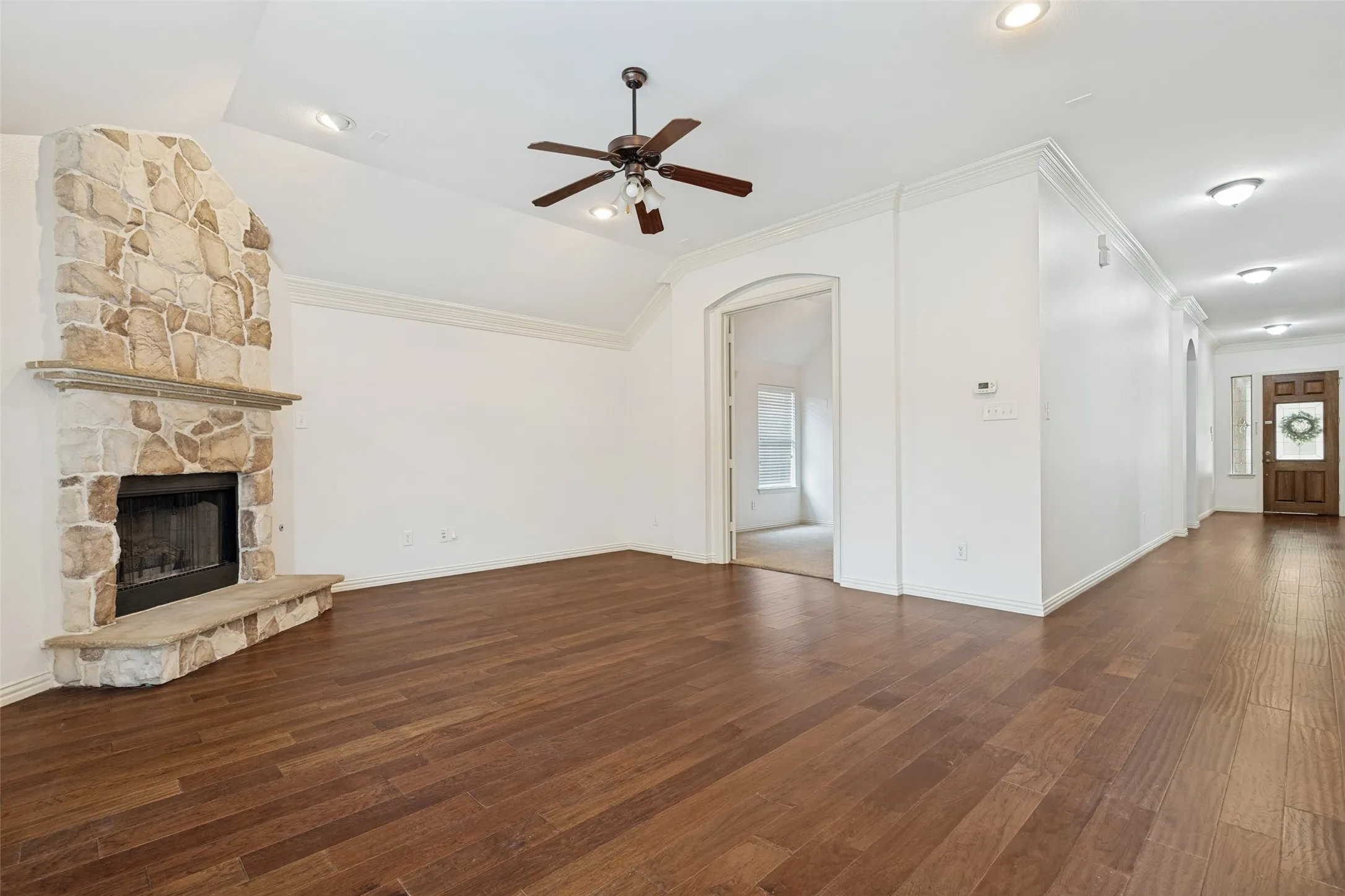 Spacious interior family room with engineered wood flooring, a stone fireplace featuring gas logs, vaulted ceiling with recessed lighting, and a ceiling fan.