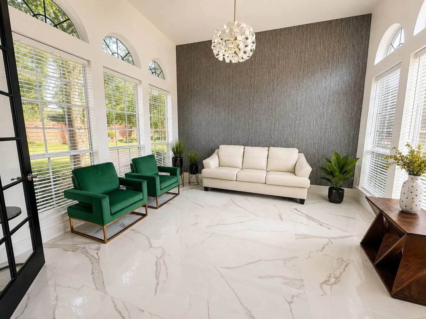 Spacious room featuring large windows with arched transoms, a textured accent wall, white marble-look flooring, and a contemporary ceiling light fixture