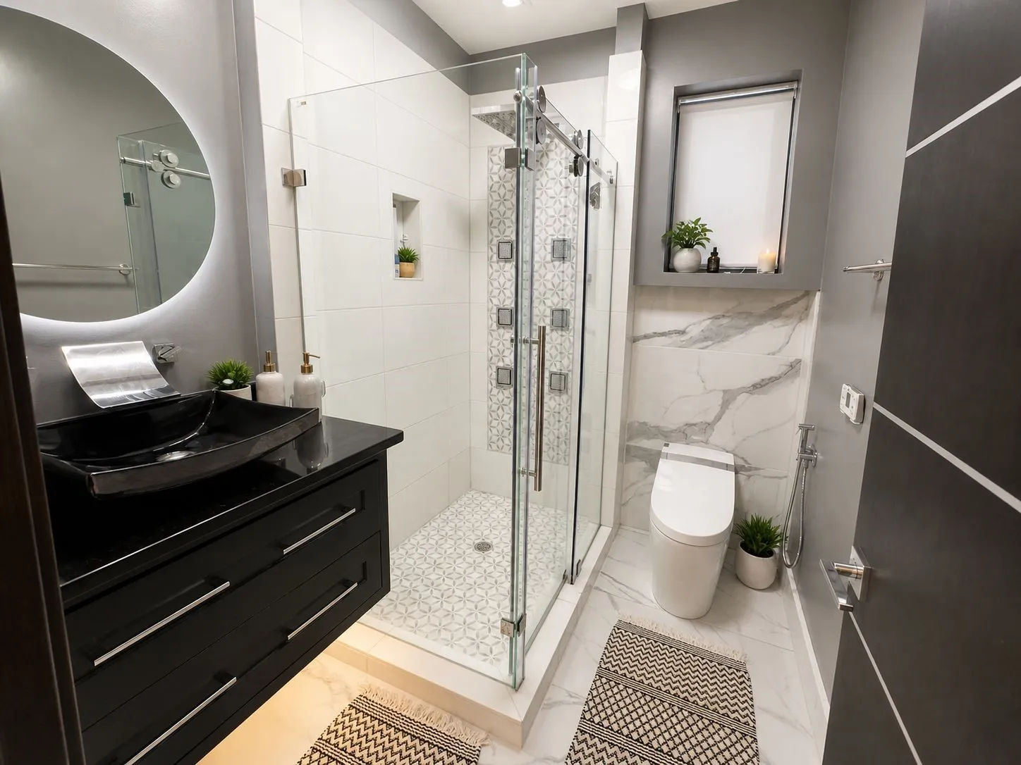 Modern bathroom featuring a frameless glass shower enclosure, a vessel sink on a dark wood-finish vanity, a backlit circular mirror, a built-in shower niche, and large format wall tiling with a natural stone pattern