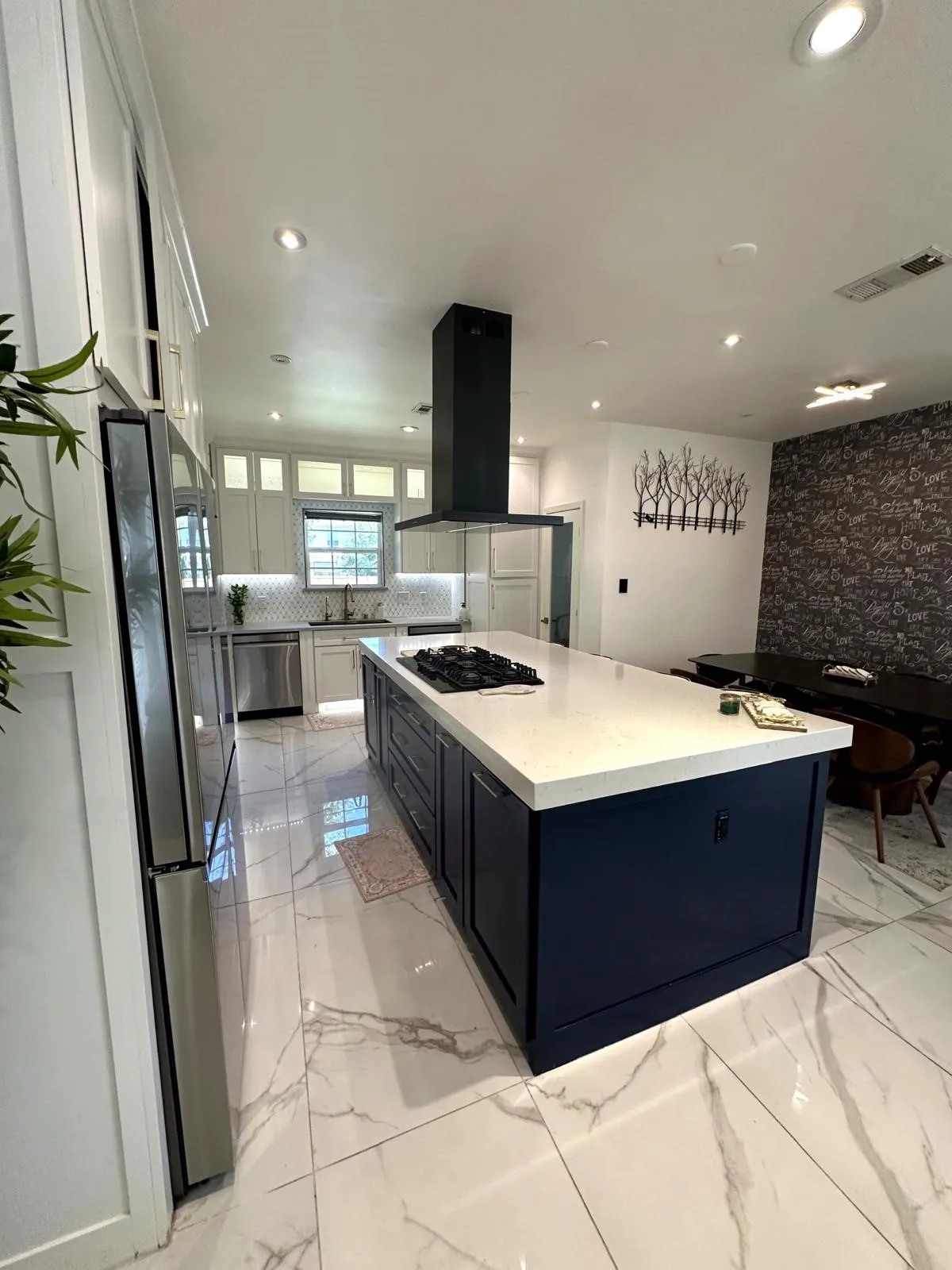 Modern kitchen featuring a large navy island with a built-in cooktop, white countertop, and stainless steel appliances
