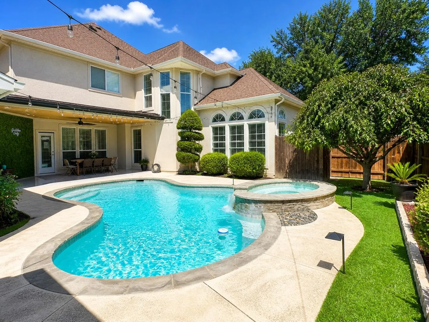 Rear exterior featuring a freeform swimming pool with integrated s pa, expansive patio, covered outdoor dining area, and manicured lawn
